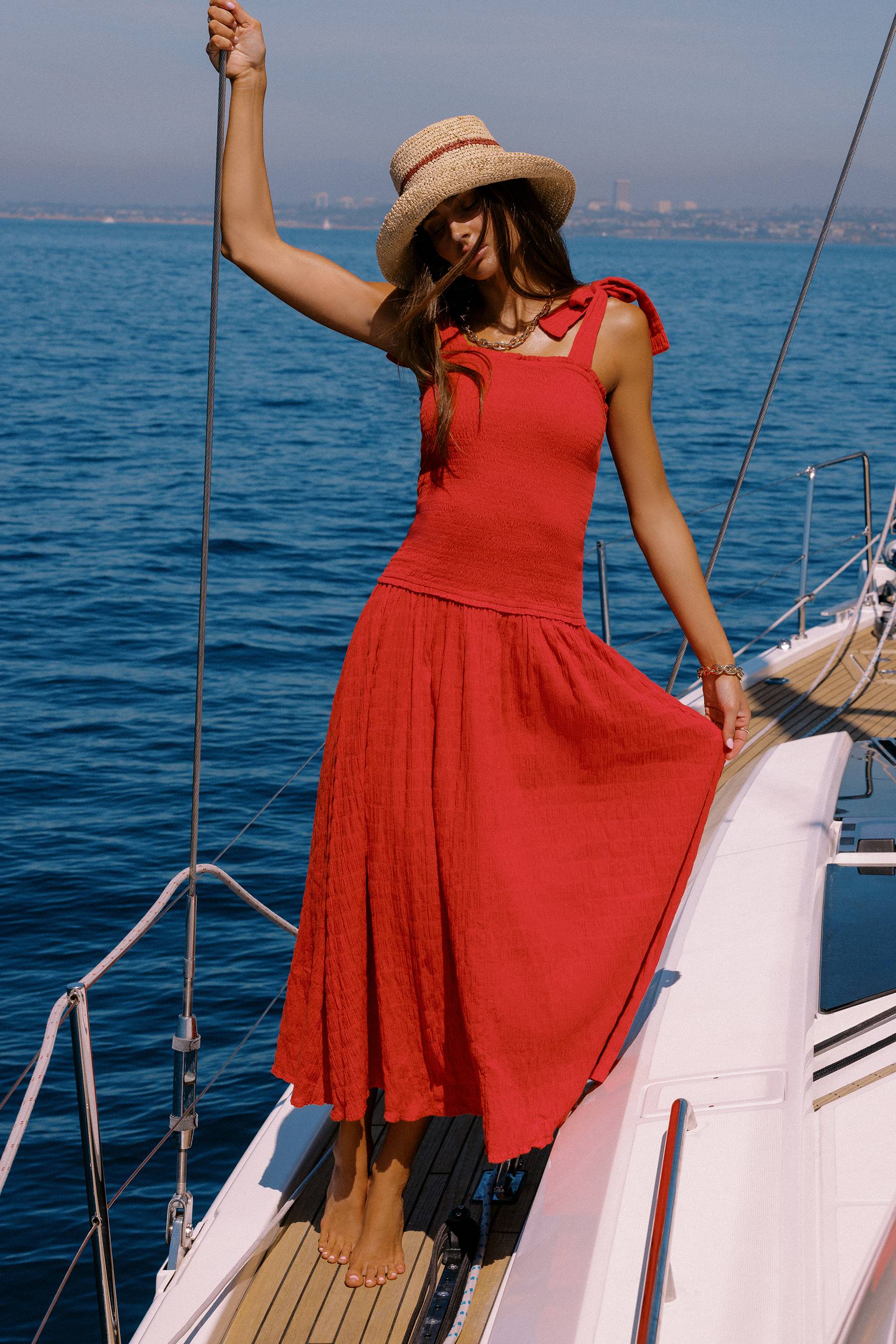 Woman in a red dress and straw hat on a sailboat with blue water and sky in the background