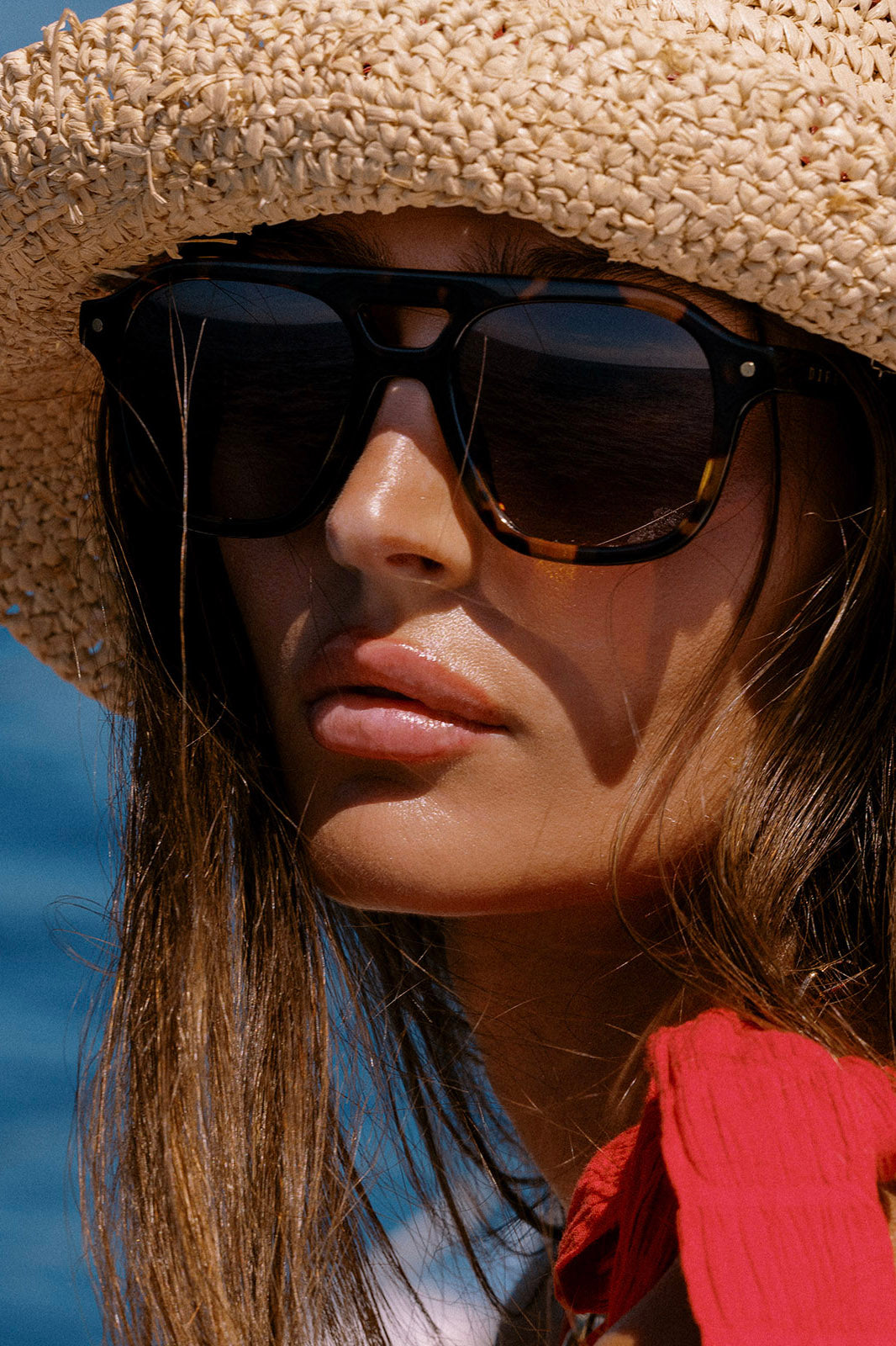 Woman wearing a straw hat and sunglasses with a blurred blue background