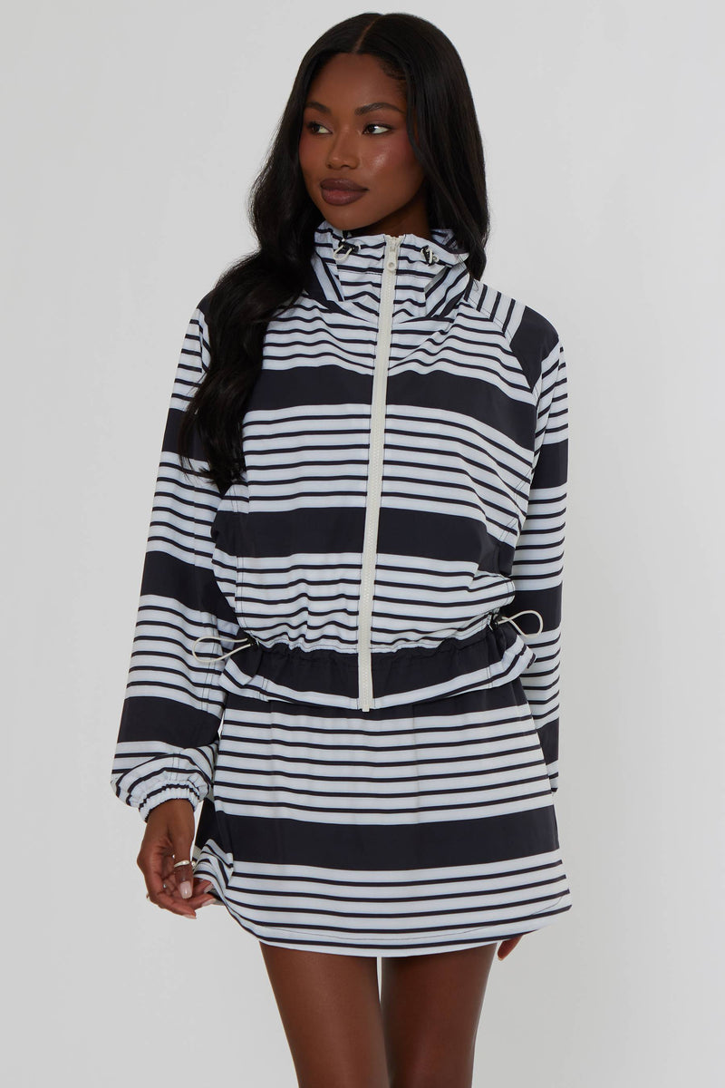 A woman modeling a black and white horizontally striped hooded zip-up jacket with a drawstring waist, photographed against a plain light gray studio background.