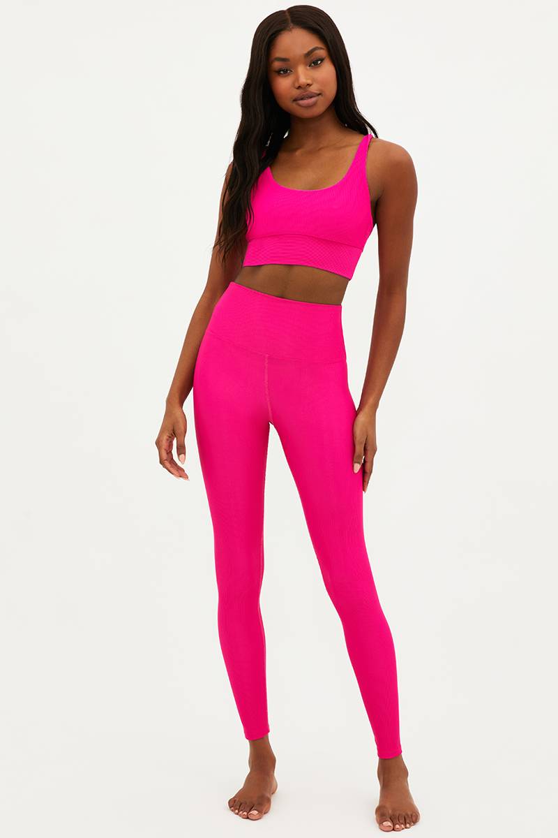 A model wearing bright fuchsia high-waisted full-length leggings with a matching sports bra.