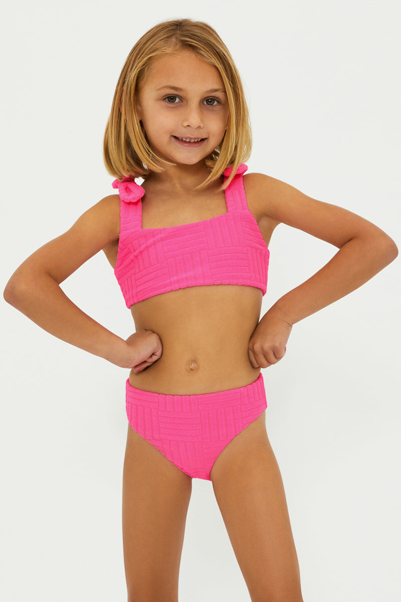 A young girl wearing a neon pink two-piece swimsuit with bows on the straps.