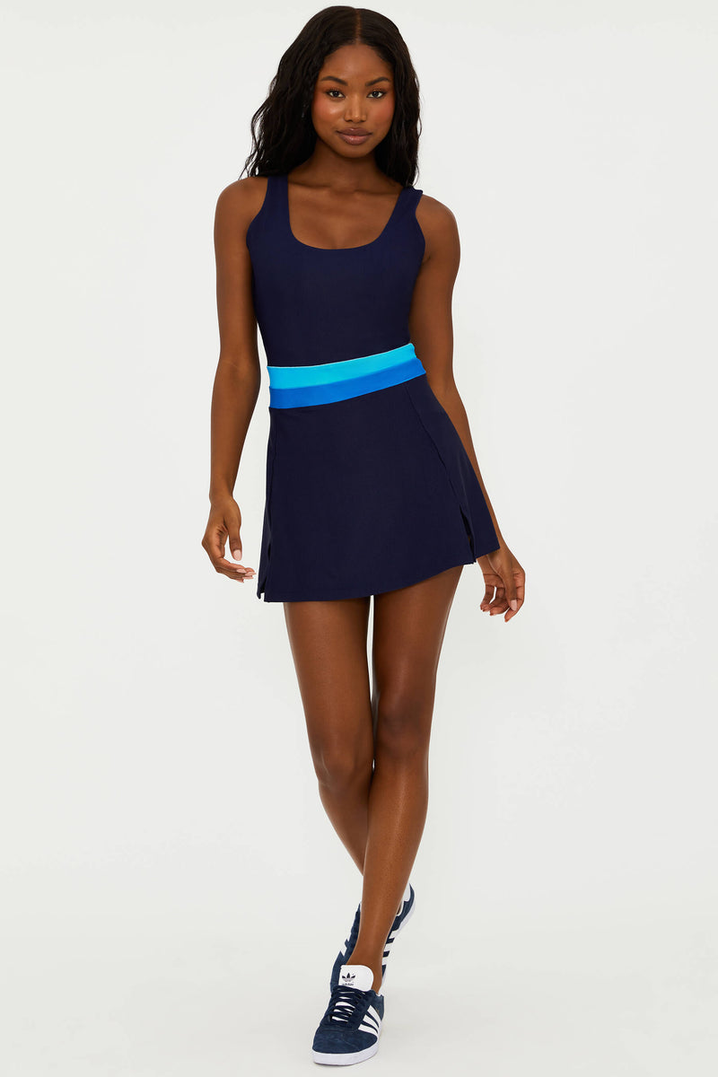 A model wearing a navy active dress with a bright blue colorblock stripe, featuring built-in shorts and a scoop neck.