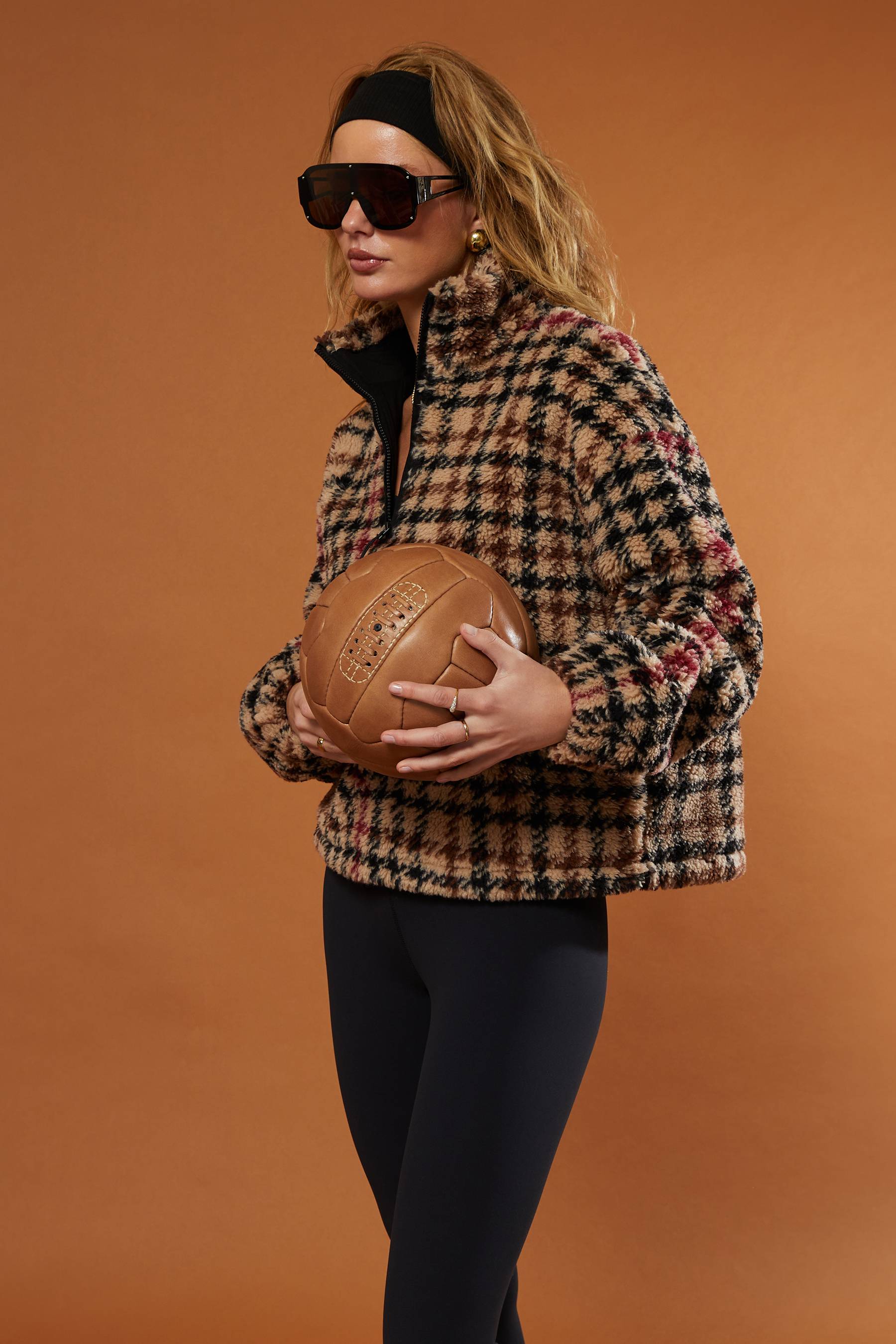 Person wearing a checkered jacket holding a leather ball against an orange background