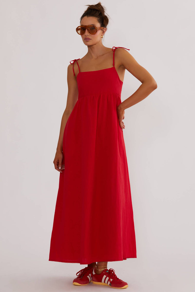 A model wearing a red maxi dress with tie shoulder straps and side pockets.