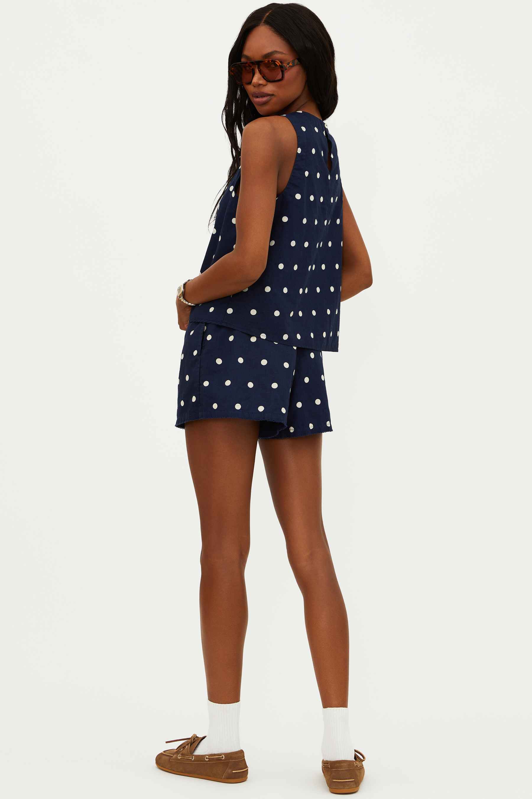 A model wearing navy shorts with white polka dots, a drawstring waistband, and side pockets.