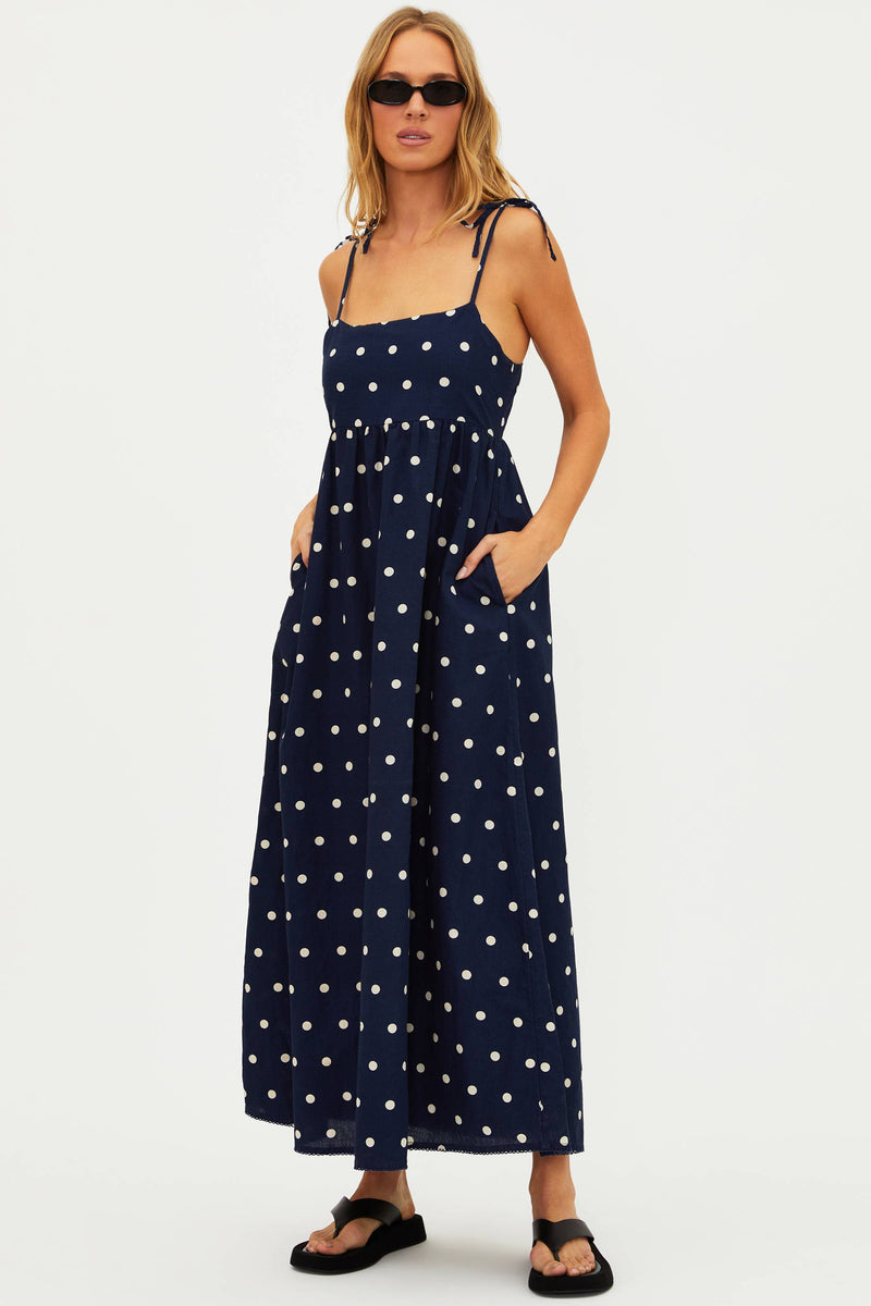 A navy maxi dress with white polka dots, featuring tie shoulder straps and side pockets.