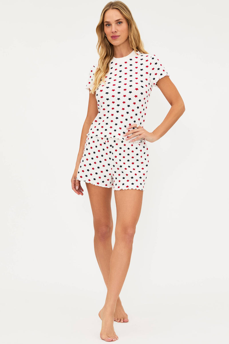 A model wearing a white sleep set with a redAmericana star pattern, featuring a short-sleeved top and matching shorts with scalloped hems.