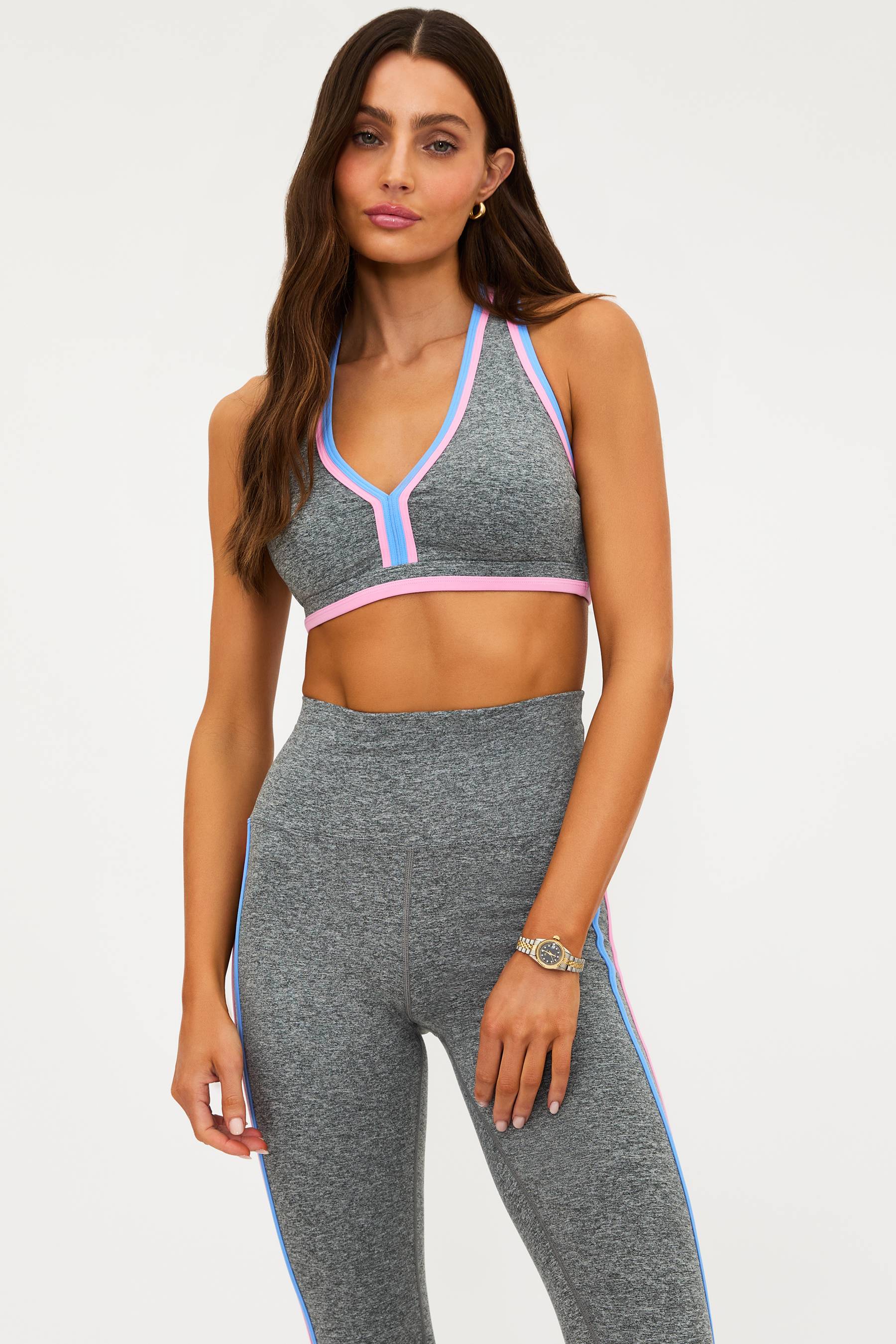 Woman wearing a gray sports bra and leggings with pink and blue accents on a white background