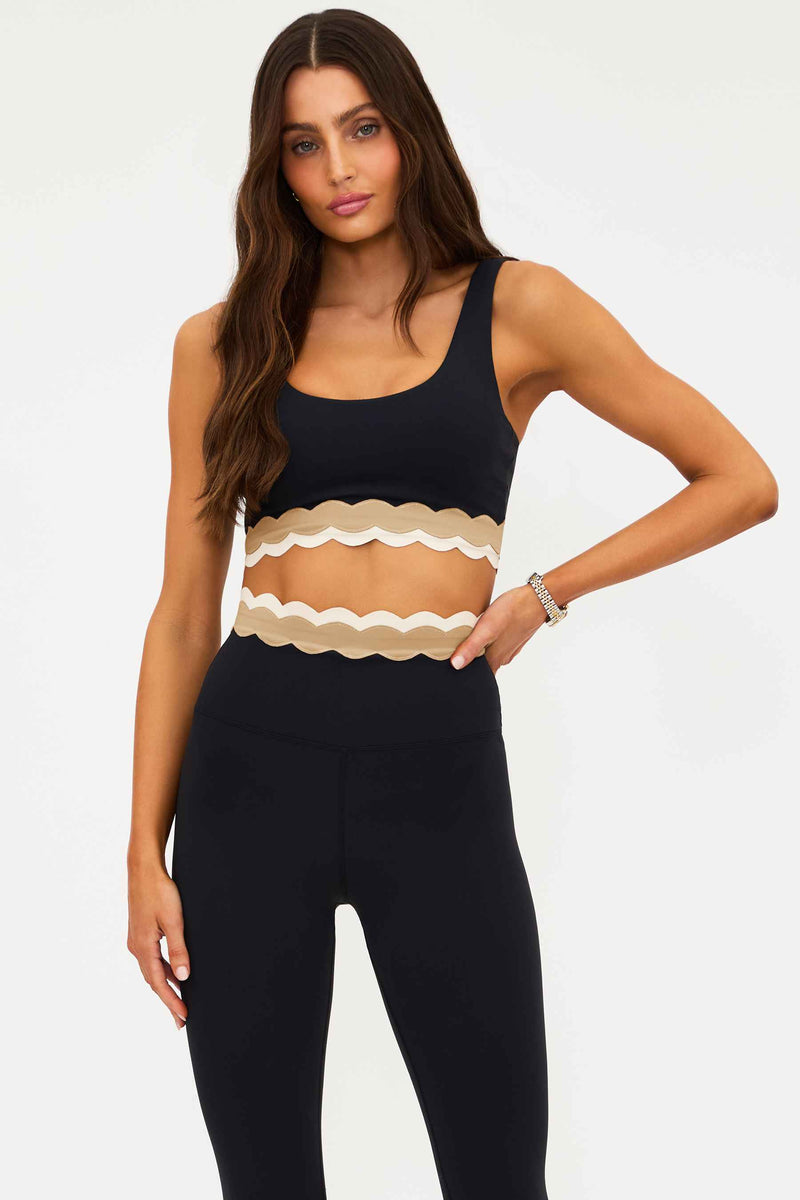 Woman wearing a black tank top with a beige ruffled design on a white background