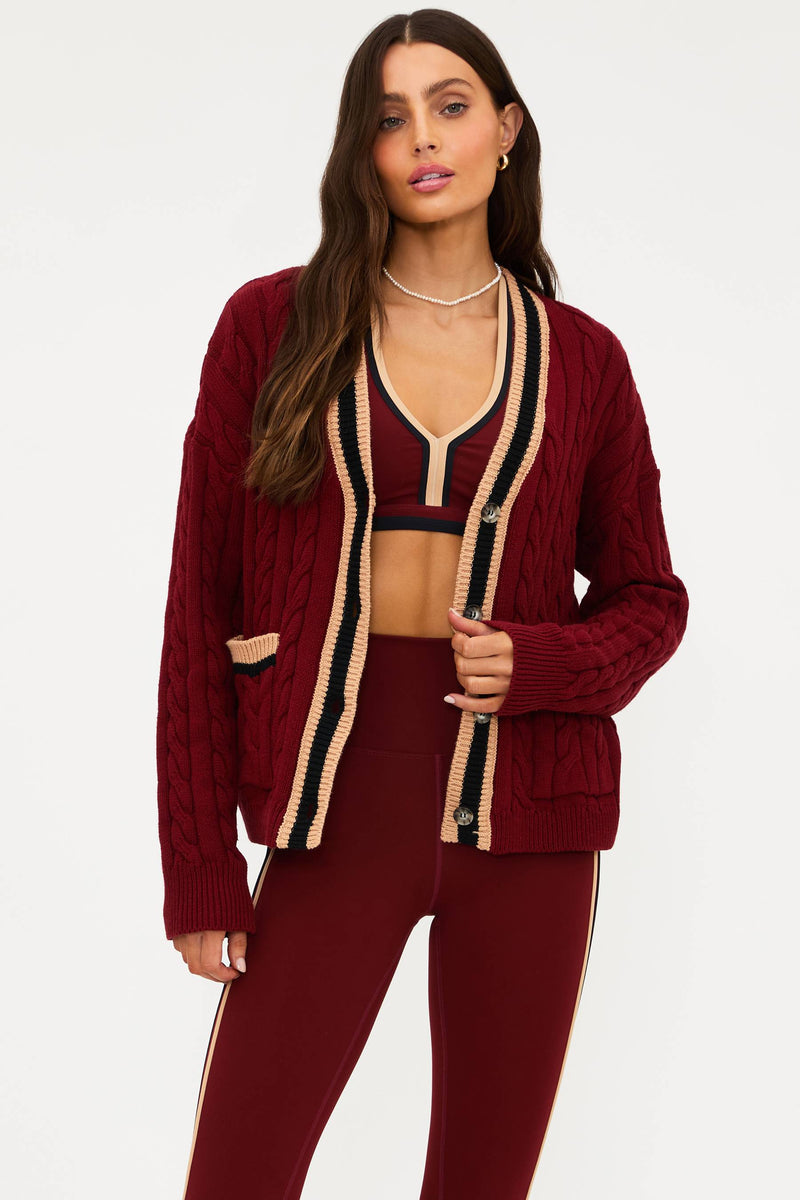Woman wearing a burgundy cardigan and pants with a white background