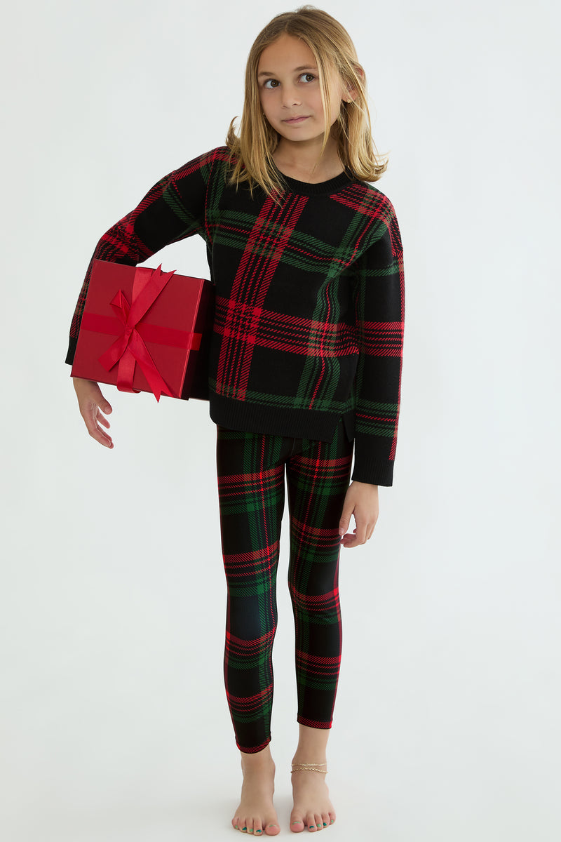 Child wearing a red and green plaid outfit holding a red gift box on a white background