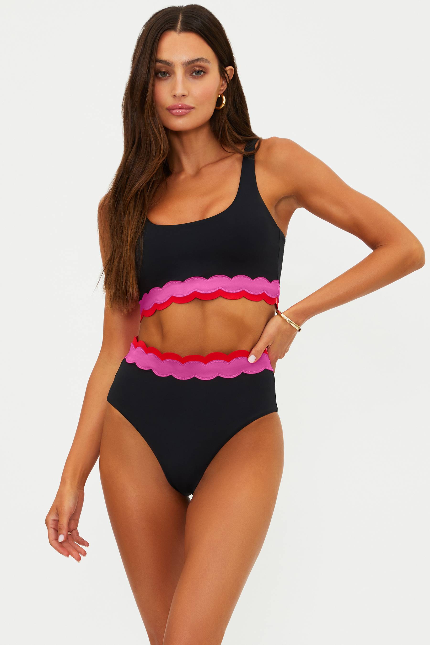 Woman wearing a black and pink swimsuit with scalloped edges on a white background