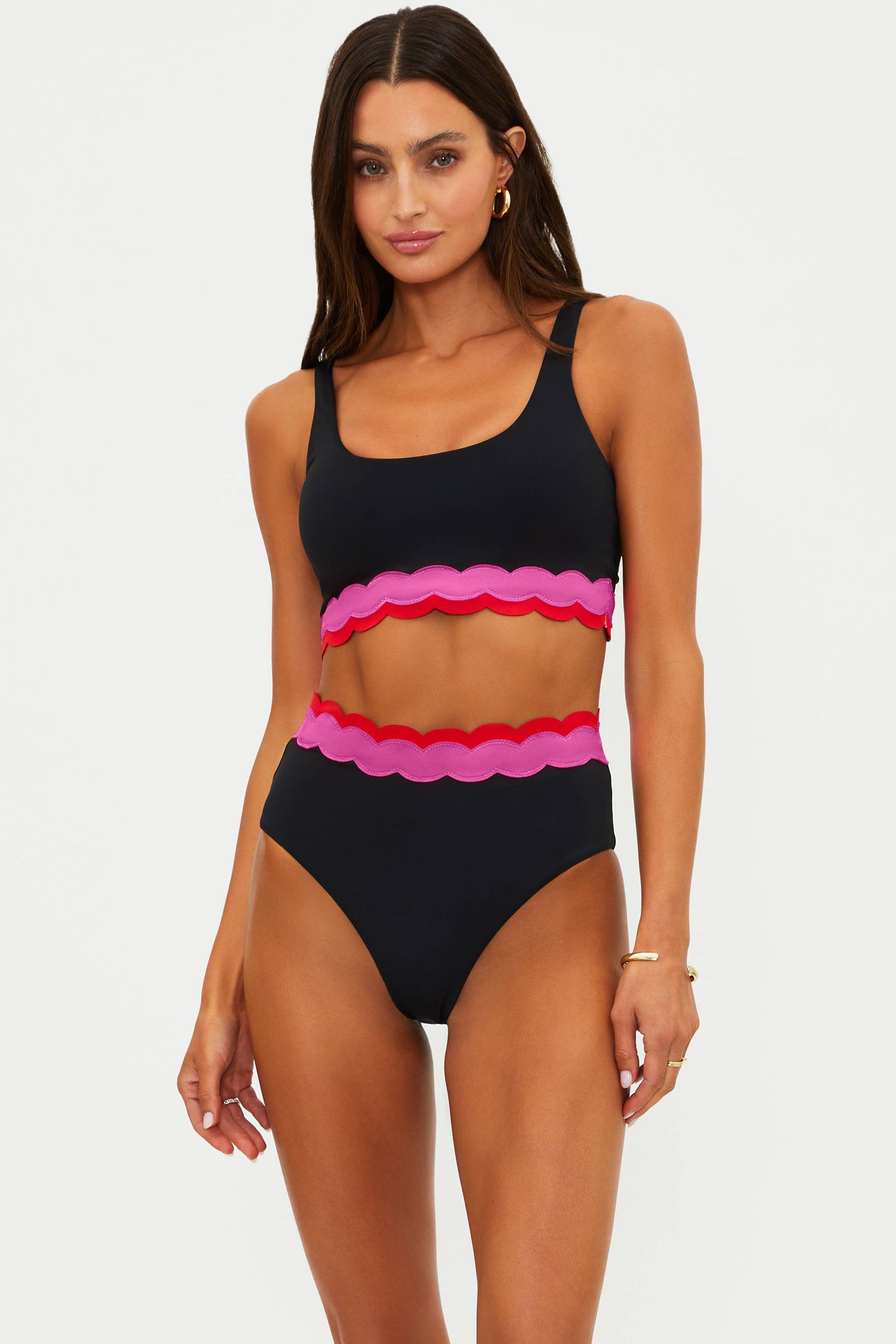 Woman wearing a black and pink bikini with scalloped edges on a white background