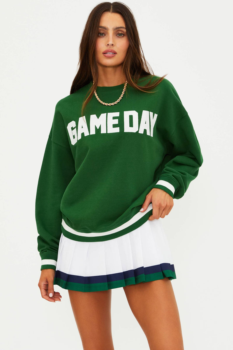 Woman wearing a green 'GAME DAY' sweatshirt and white skirt with green trim on a white background