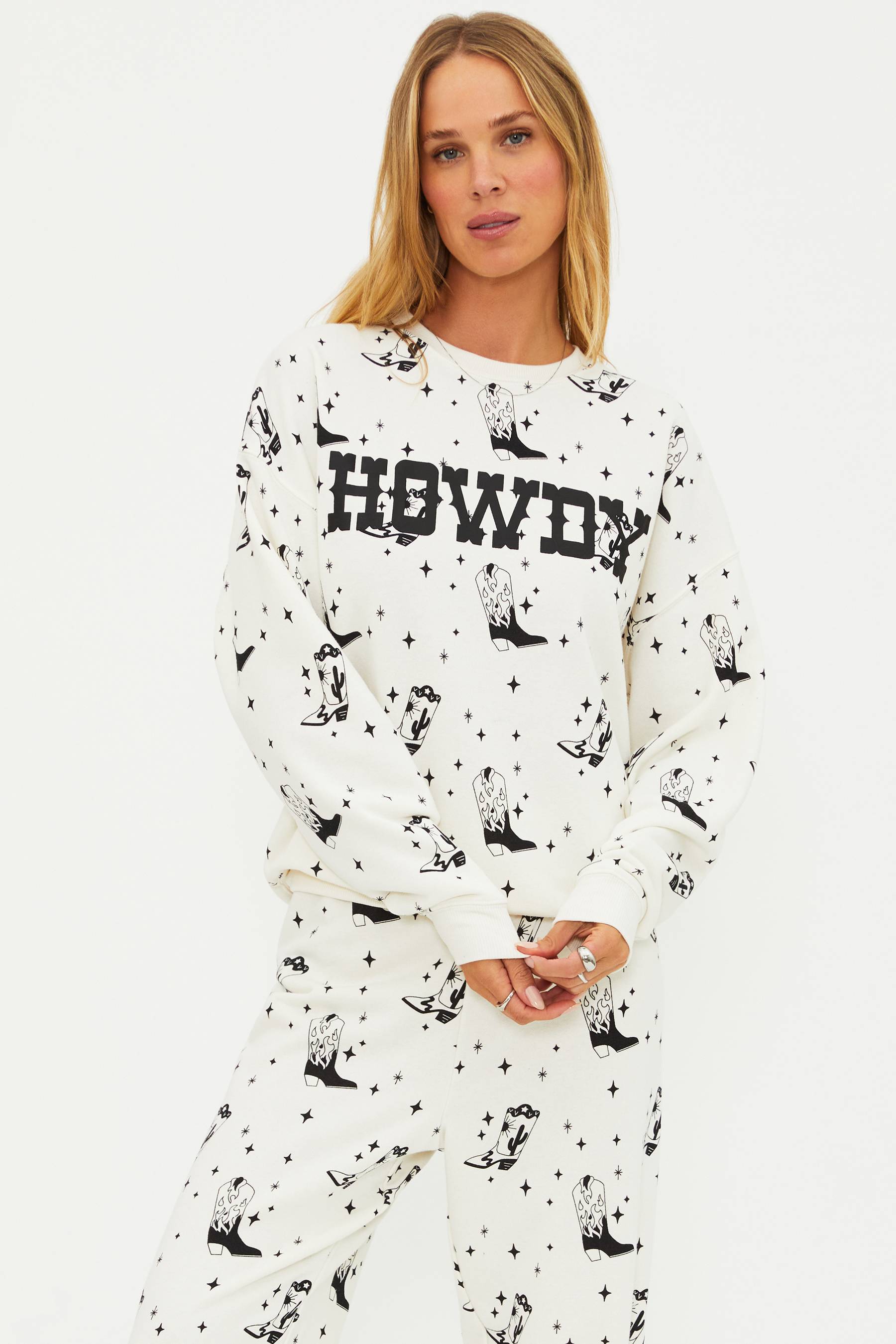 Woman wearing a white pajama set with black patterns and 'HOWDY' text on a plain background