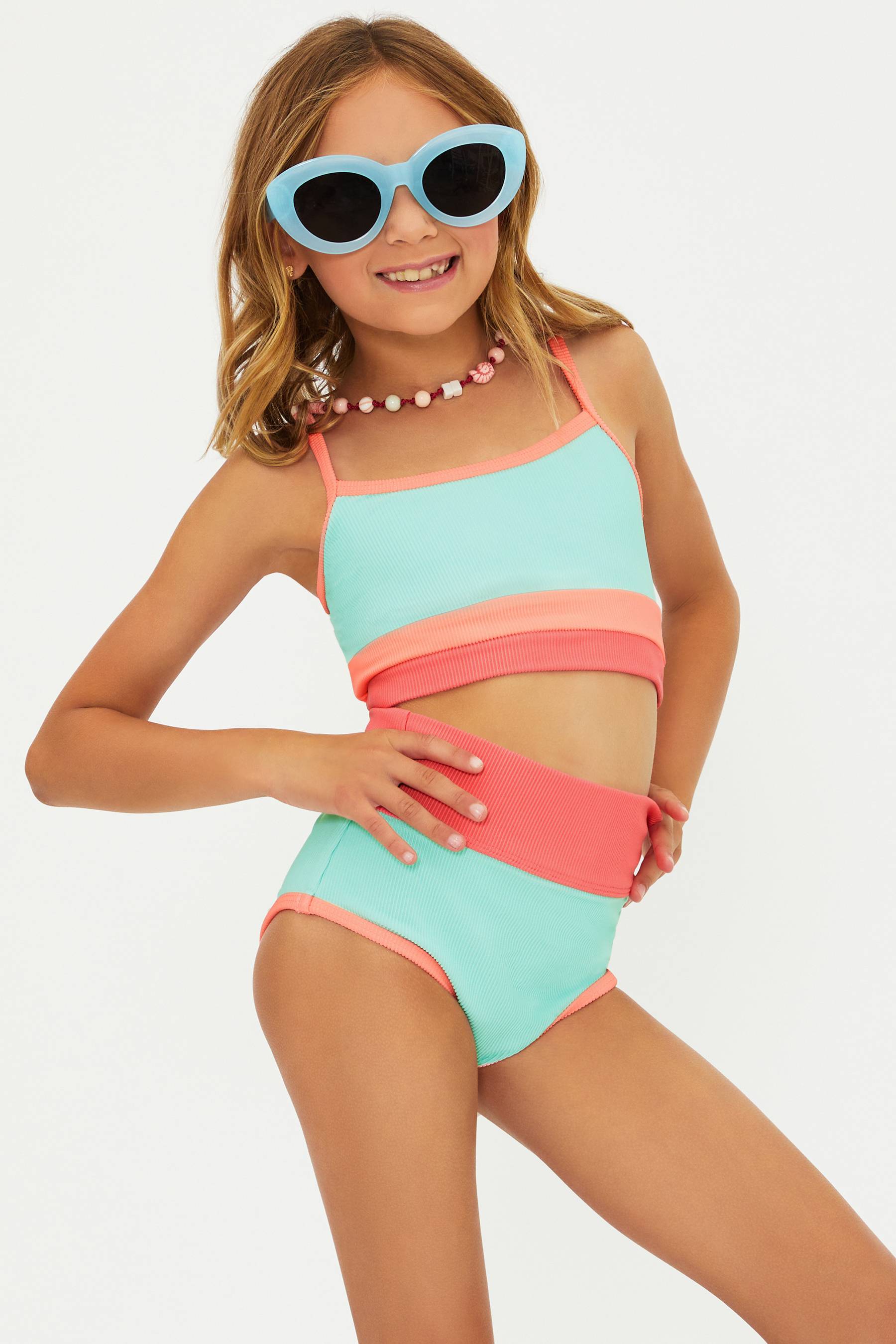 Young girl wearing a colorful two-piece swimsuit and sunglasses on a white background
