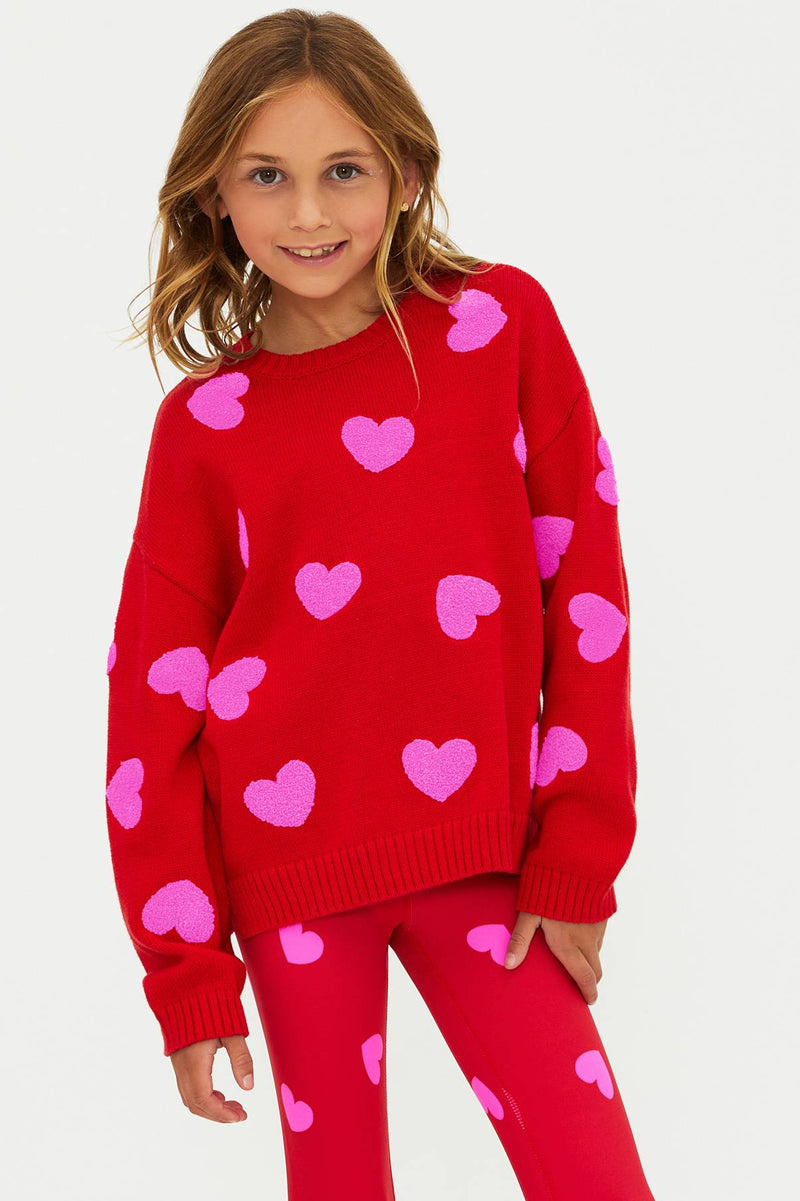 Child wearing a red sweater and leggings with pink heart patterns on a white background