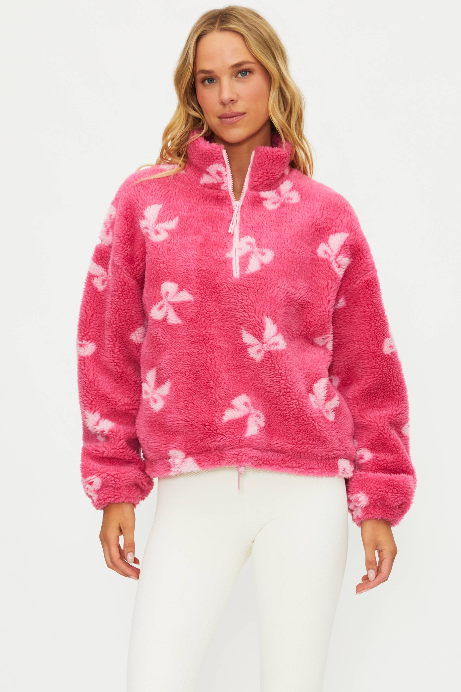 Woman wearing a pink fleece pullover with white bow patterns on a white background