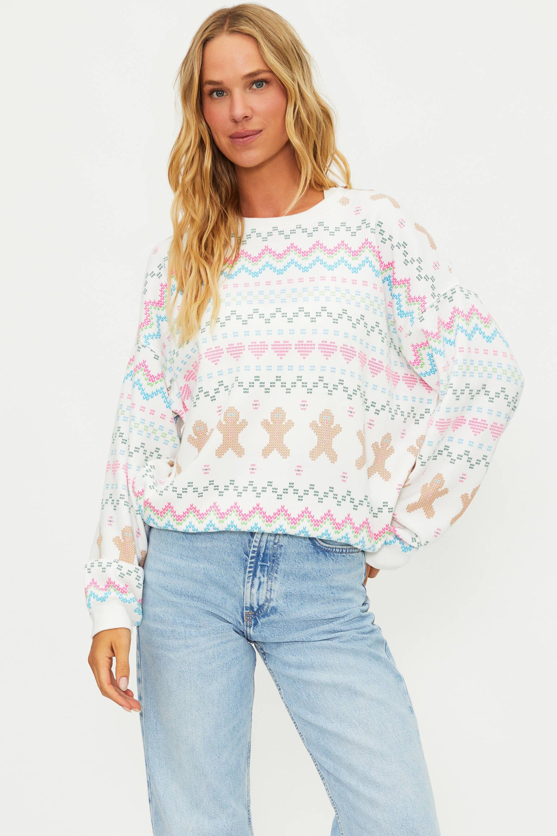 Woman wearing a colorful sweater with gingerbread men design and light blue jeans on a white background