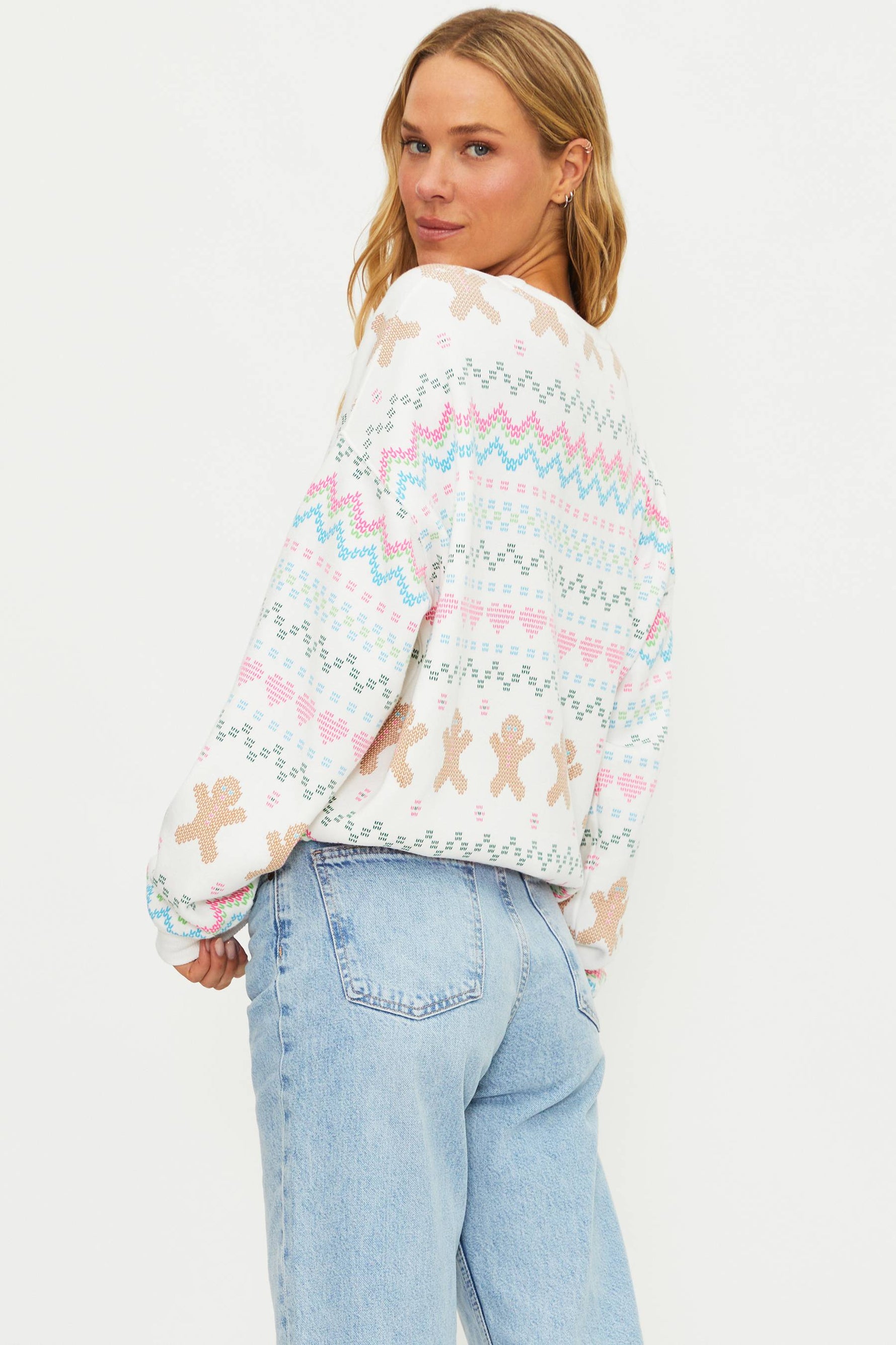 Person wearing a colorful sweater with gingerbread patterns on a plain background