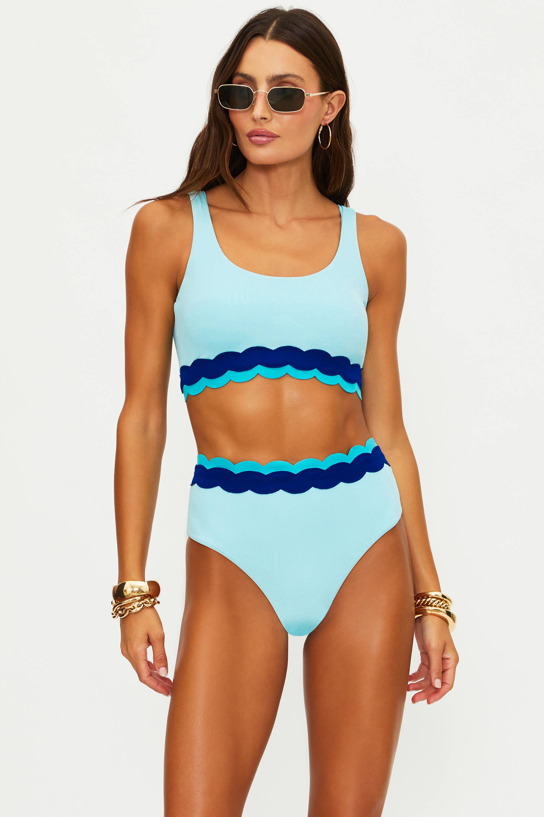 Woman wearing a light blue and dark blue swimsuit with sunglasses on a white background