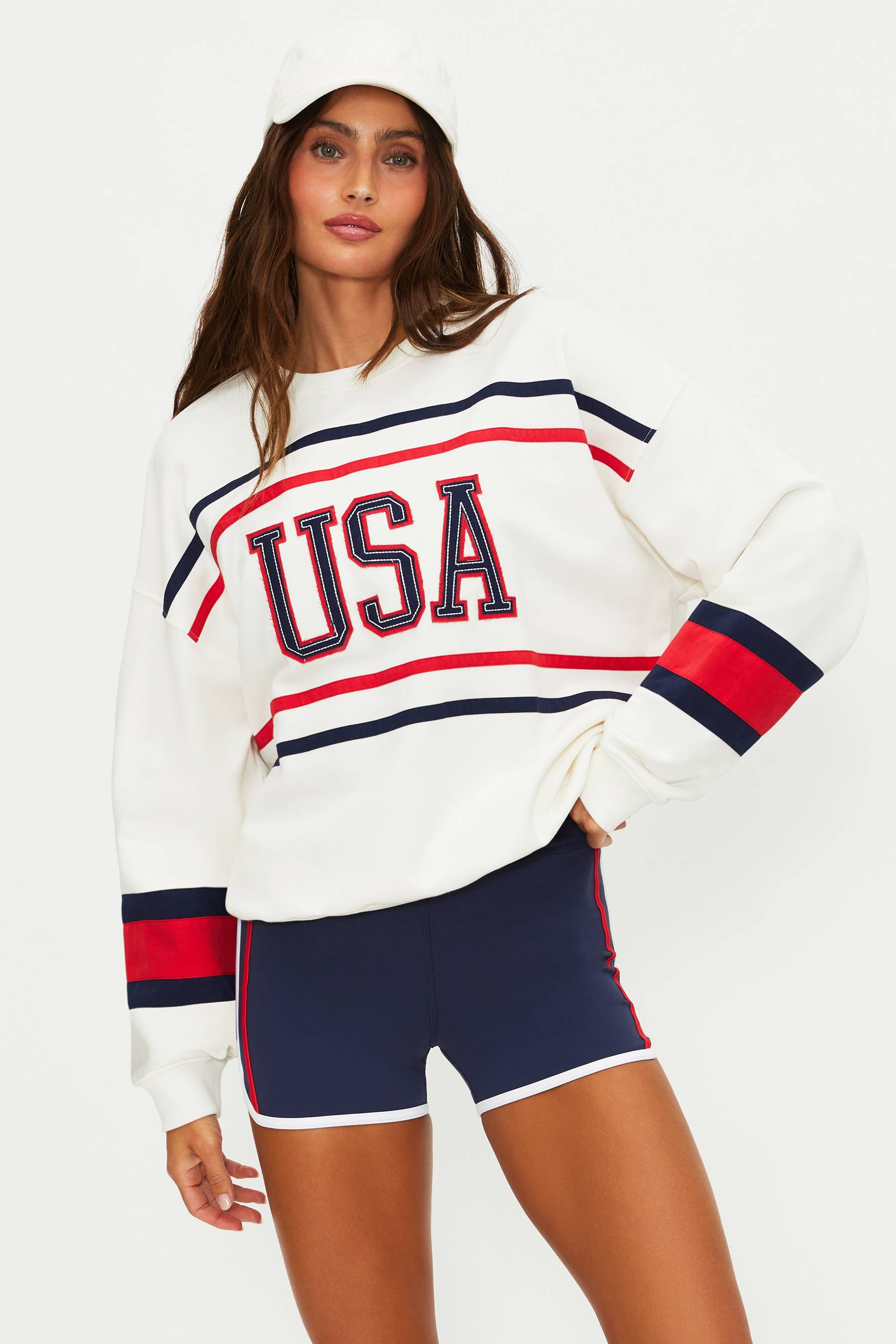 Woman wearing a white sweatshirt with 'USA' text and navy shorts on a white background