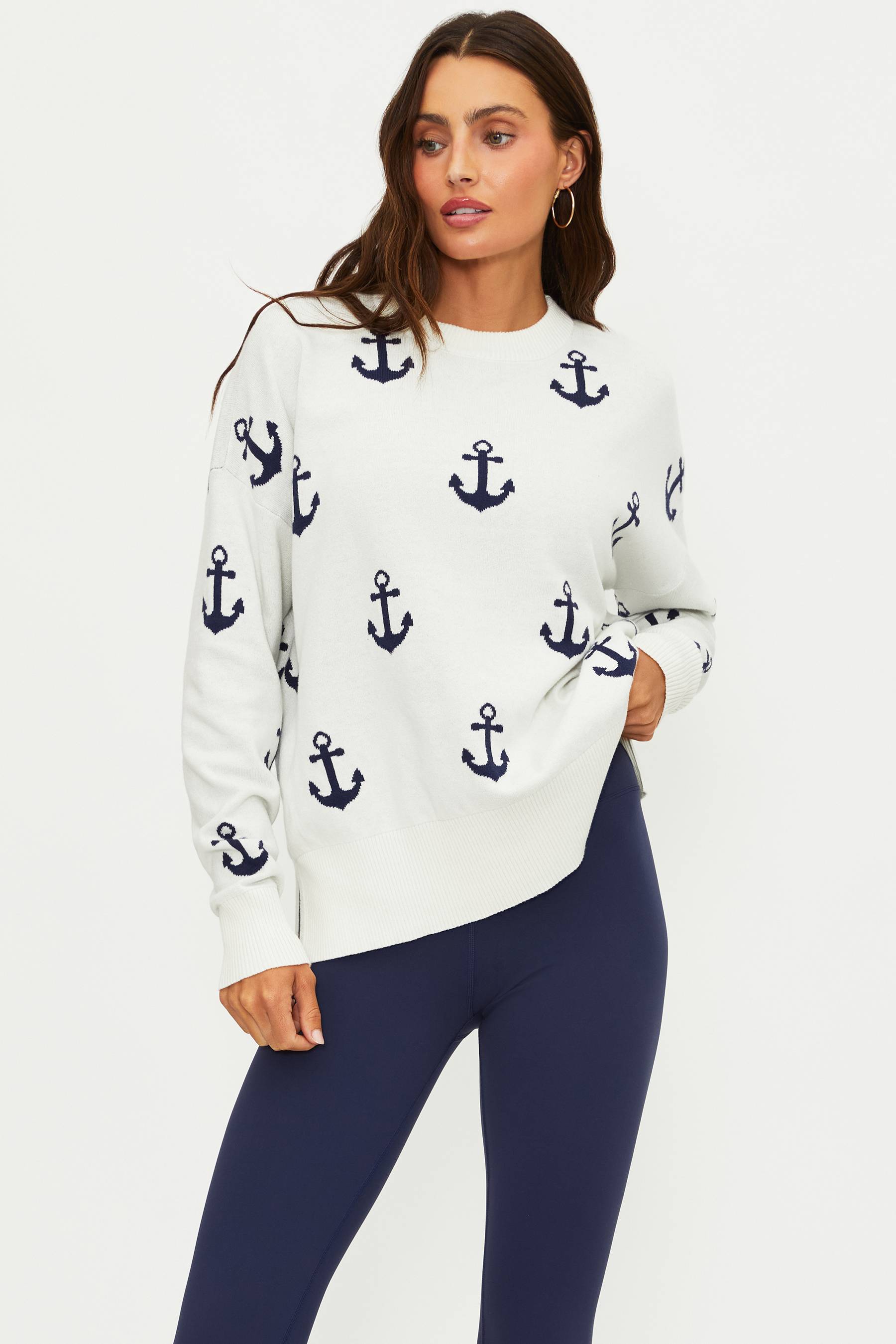 Woman wearing a white sweater with anchor patterns and dark blue leggings on a light gray background