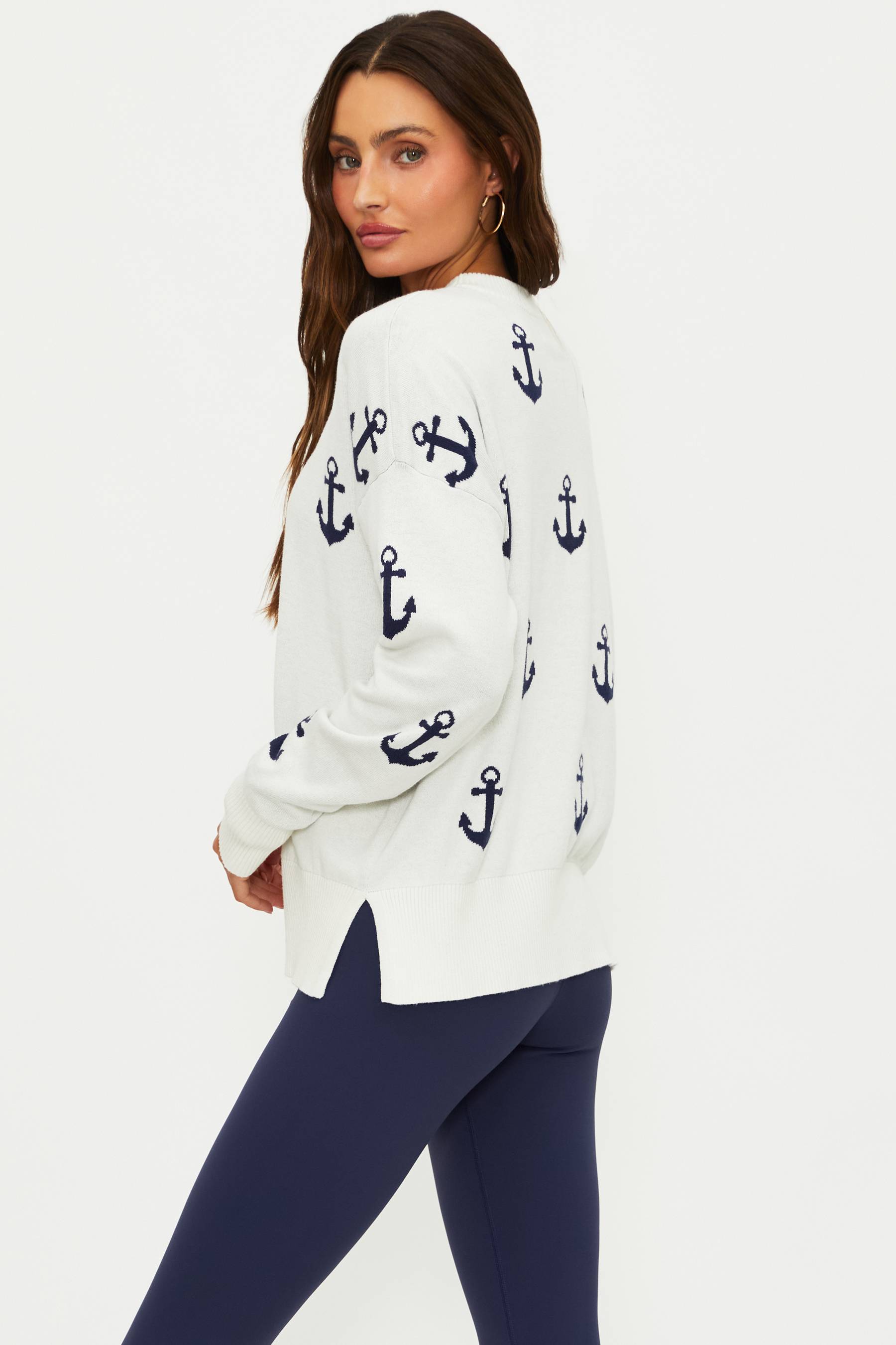 Woman wearing a white sweater with anchor patterns on a plain background