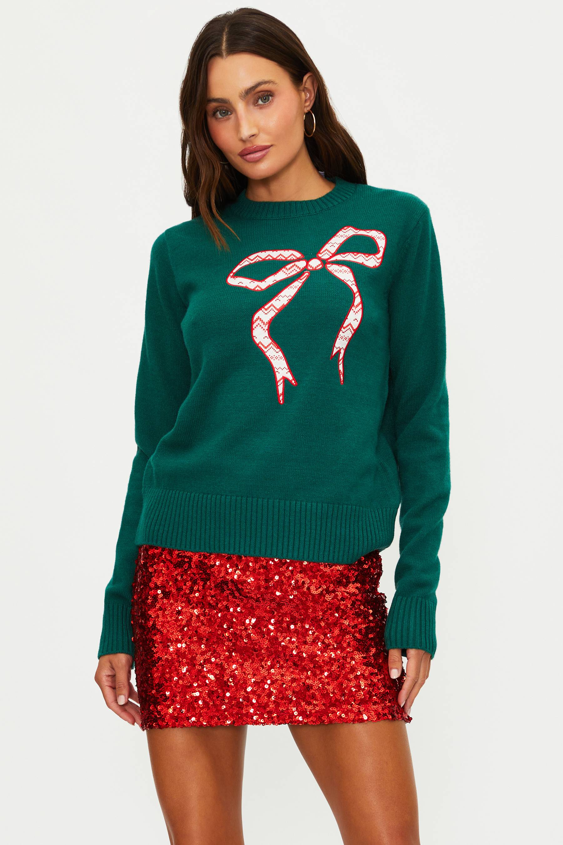 Woman wearing a green sweater with a red bow design and a red sequin skirt on a white background
