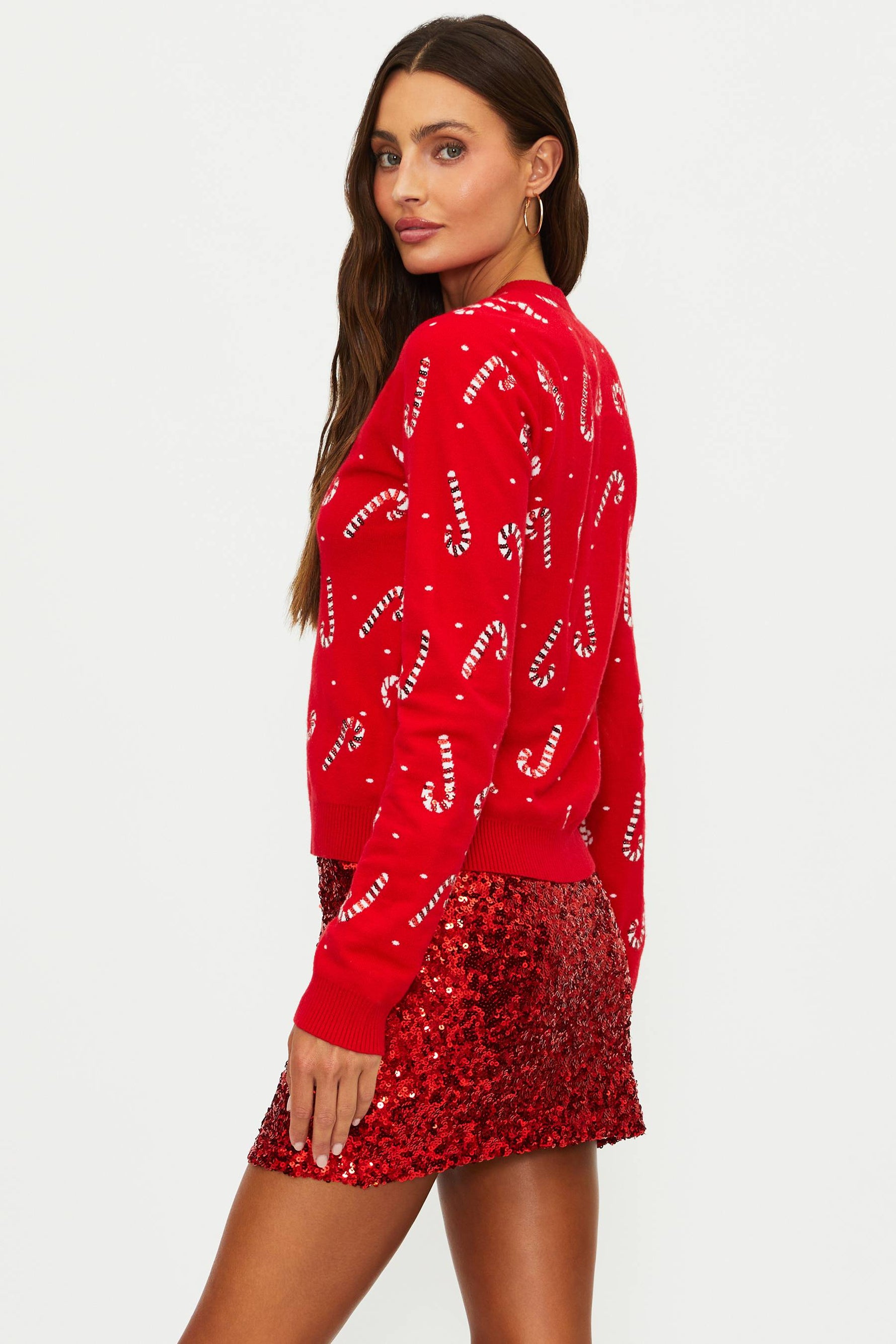 Woman wearing a red sweater with candy cane pattern and a matching red sequin skirt on a white background