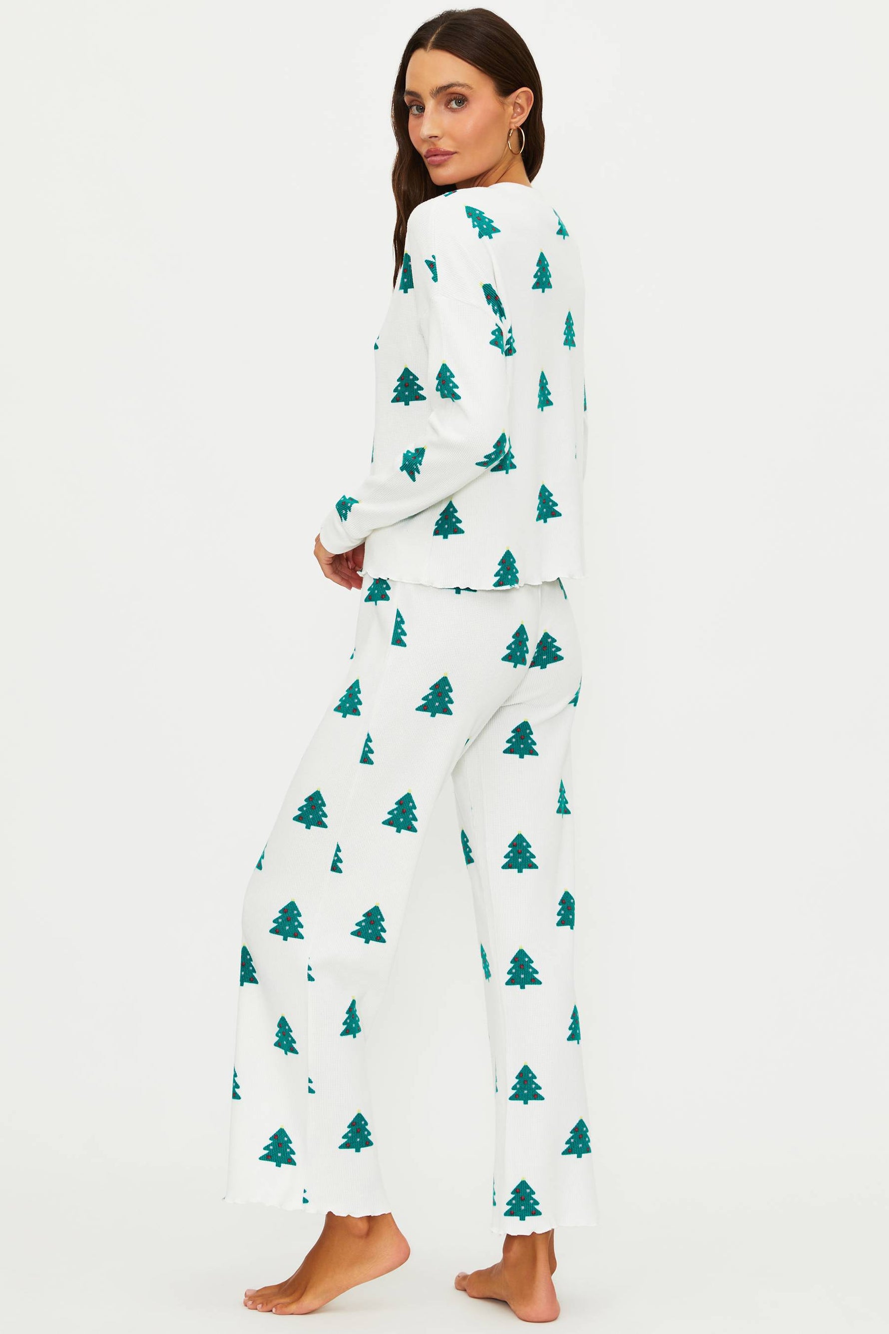 Woman wearing a white pajama set with green tree patterns on a white background