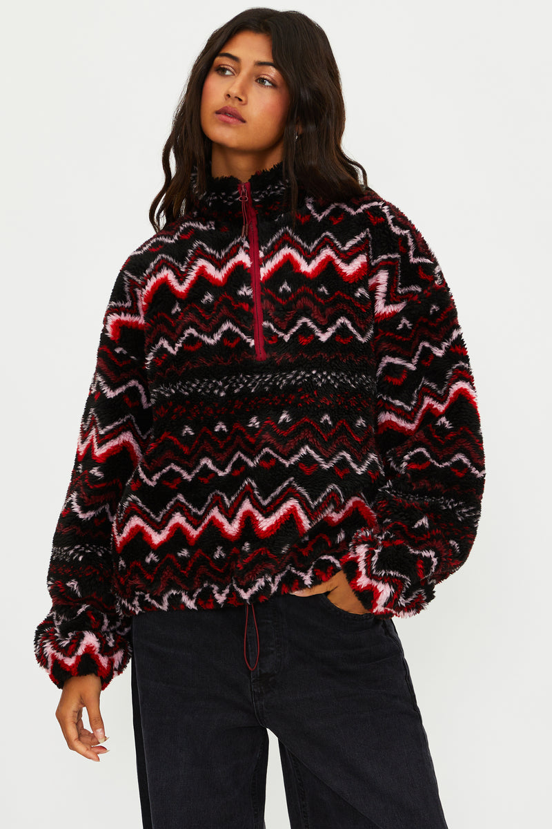 Person wearing a patterned sweater with red and black design on a white background