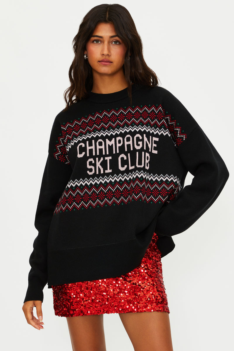 Woman wearing a black sweater with 'Champagne Ski Club' text and a red sequin skirt on a white background
