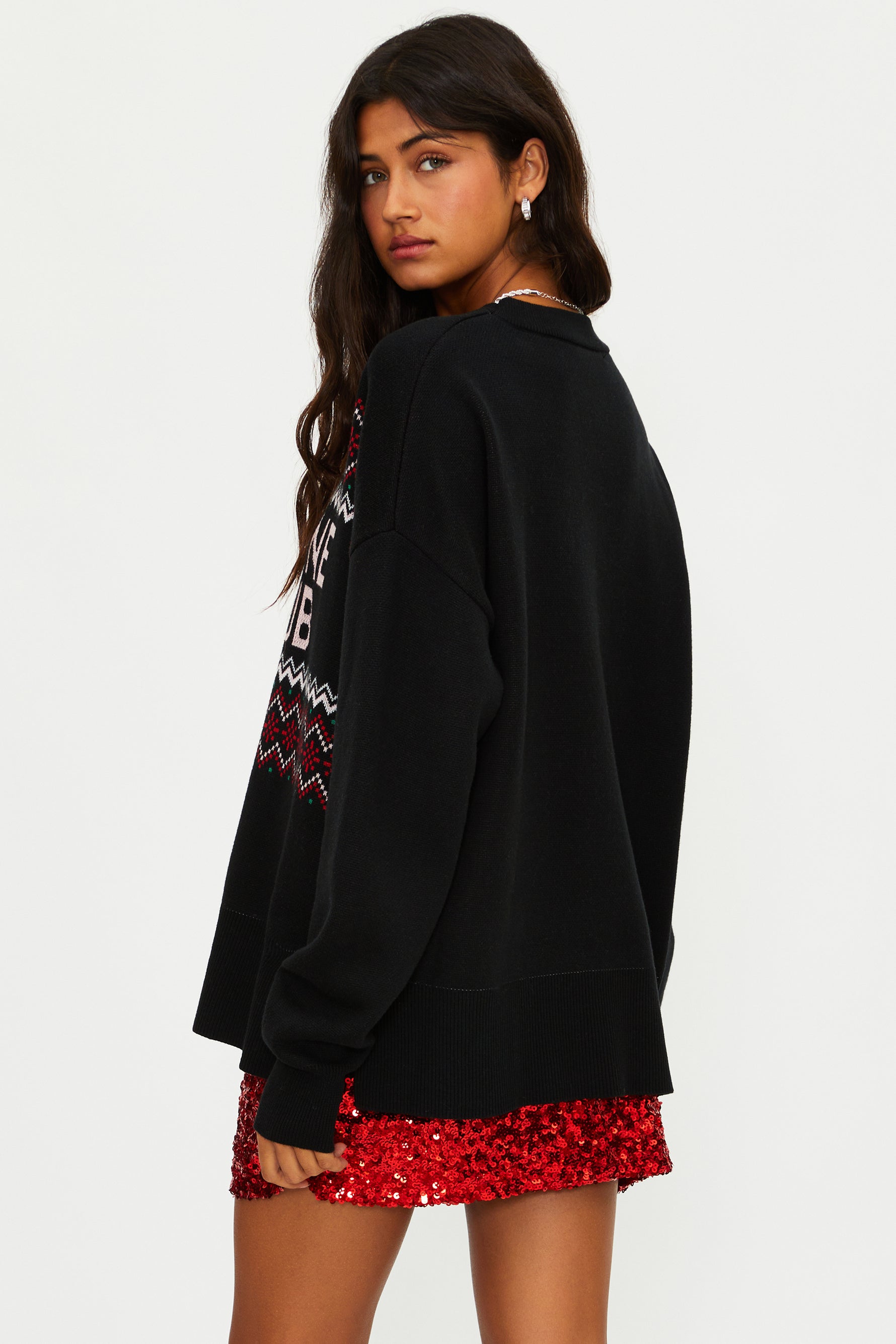 Woman wearing a black sweatshirt with a colorful design and a red sequin skirt on a white background