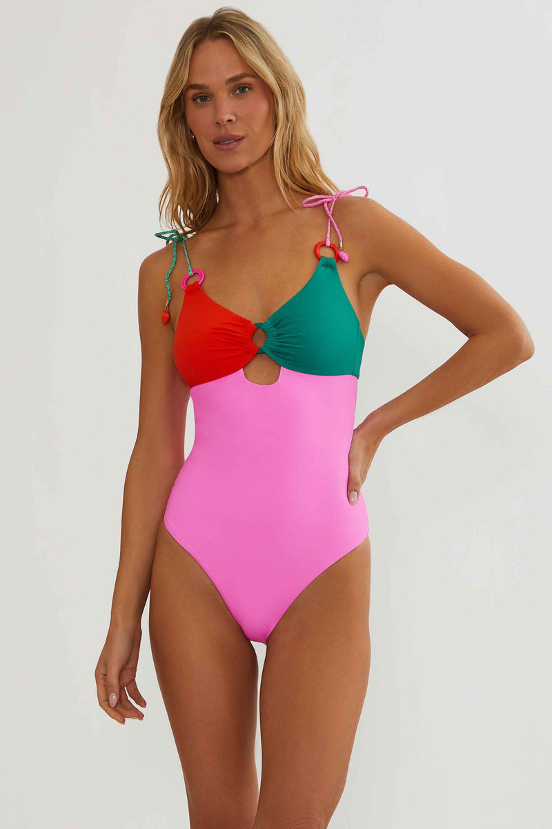 Woman wearing a colorful one-piece swimsuit with red, green, and pink sections on a white background.
