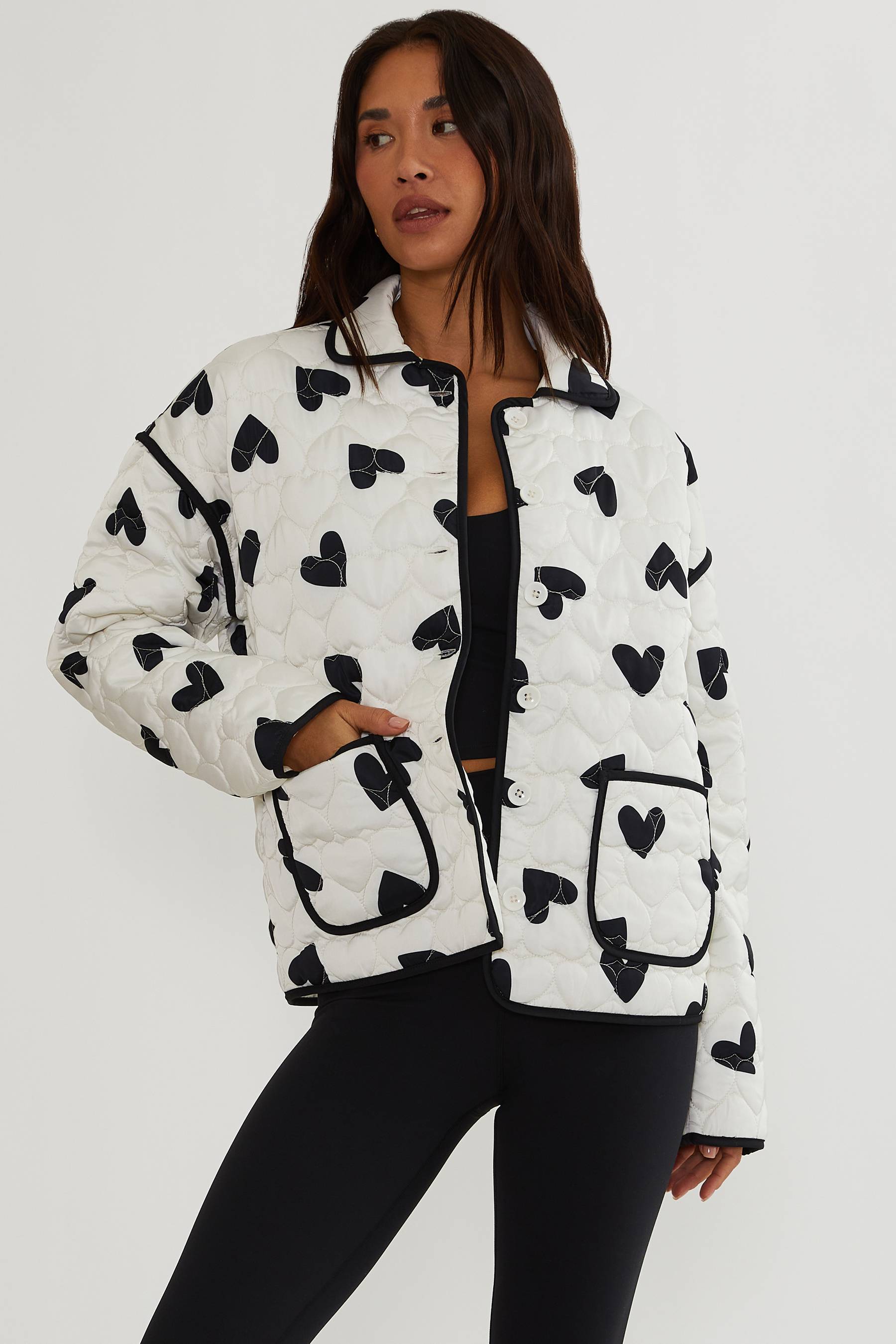 Woman wearing a white puffer jacket with black heart patterns on a white background