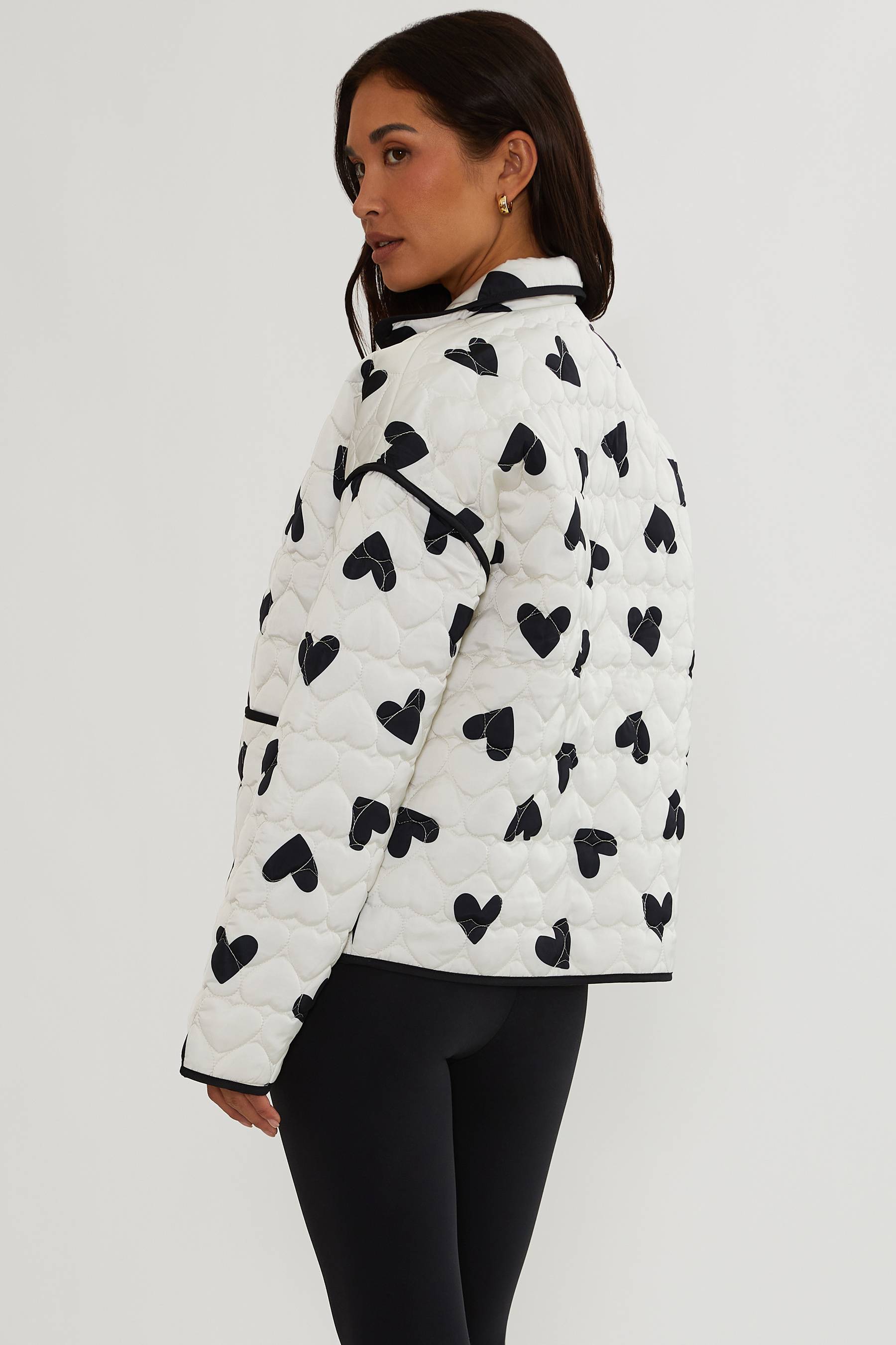 Person wearing a white puffer jacket with black heart patterns on a plain background