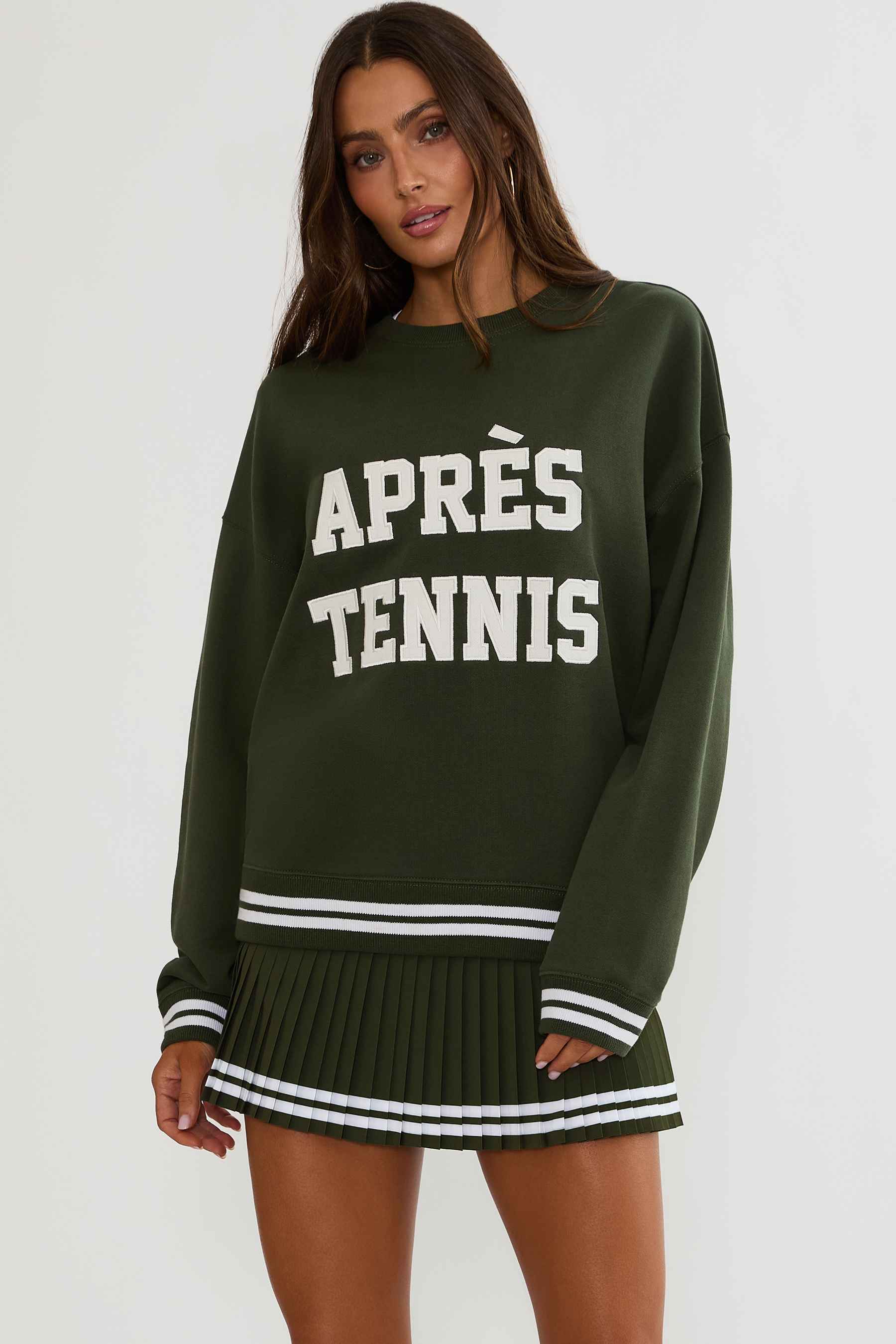 Woman wearing a green sweatshirt with white text "apres tennis"