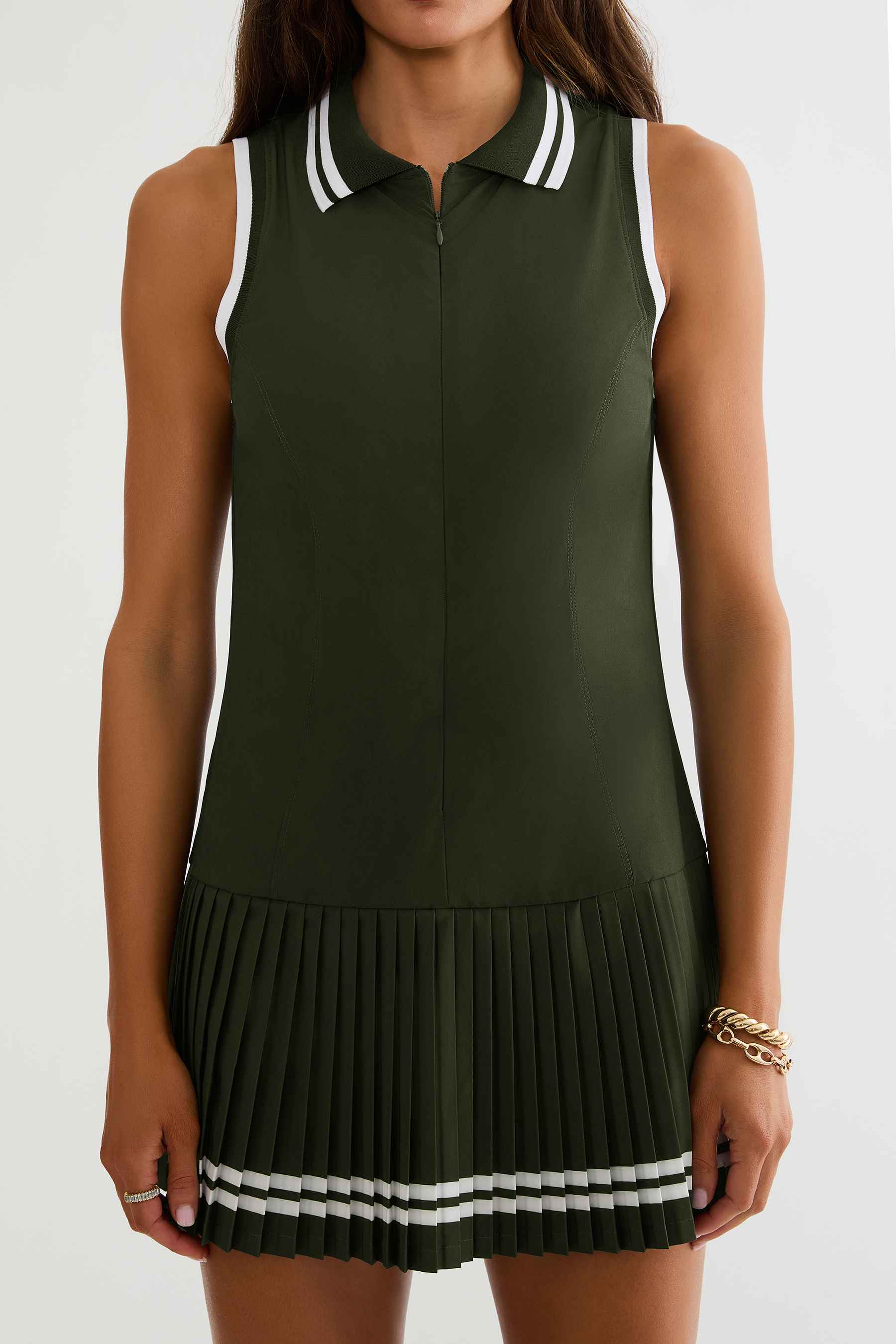 Woman wearing olive green tennis dress with white detailing on a white background. 