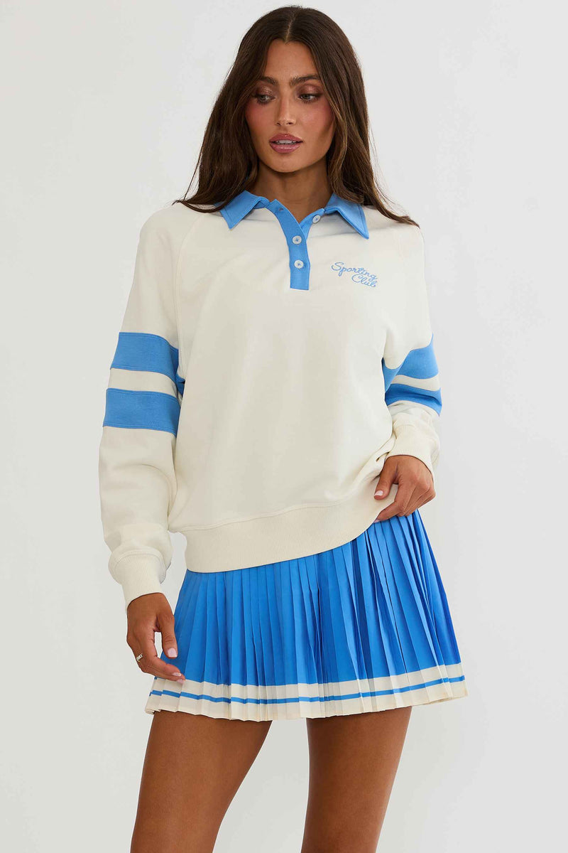 Woman wearing cream and blue polo sweater with "sports club" text on the chest.
