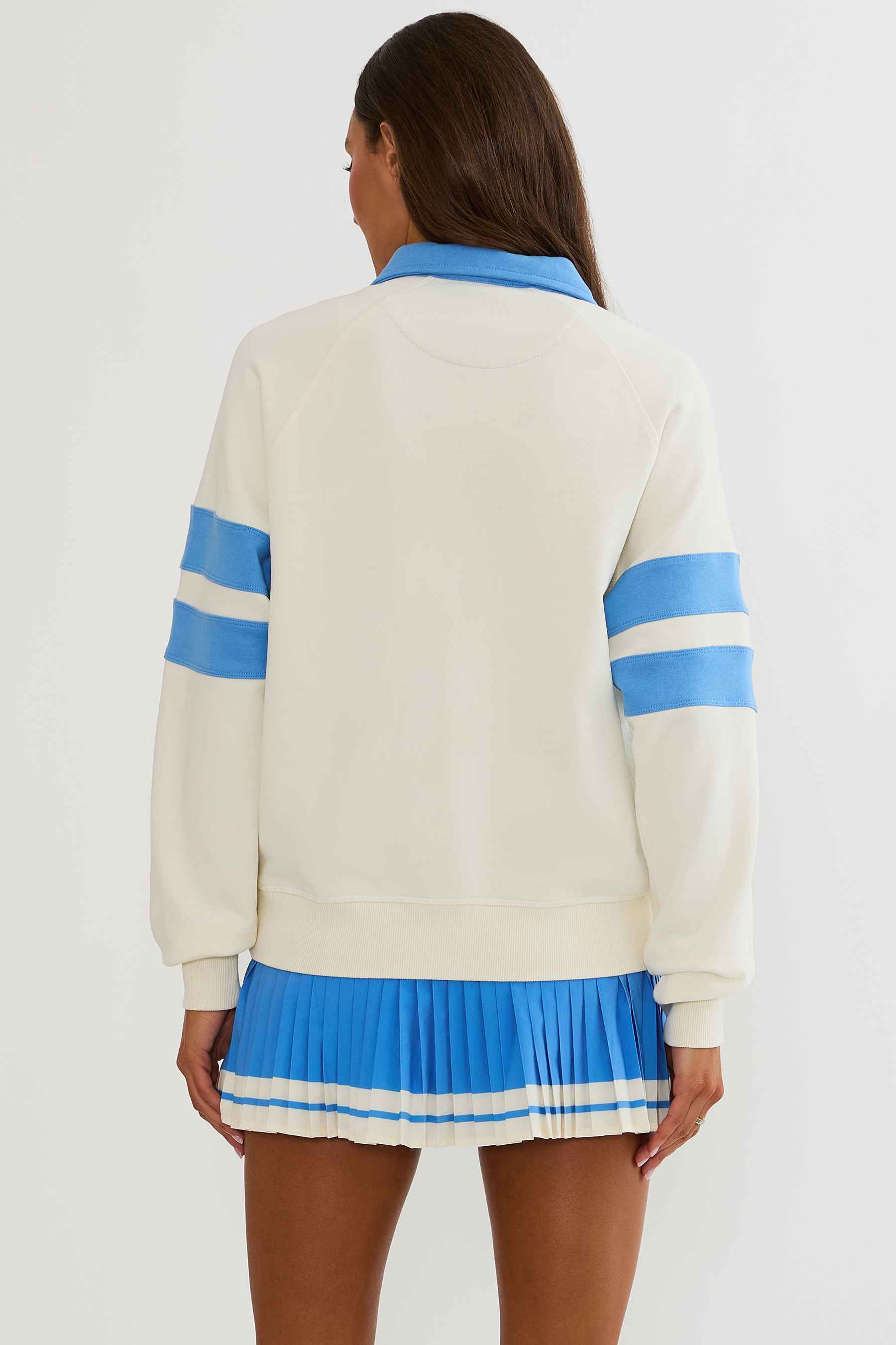 Woman wearing cream and blue polo sweater with "sports club" text on the chest.