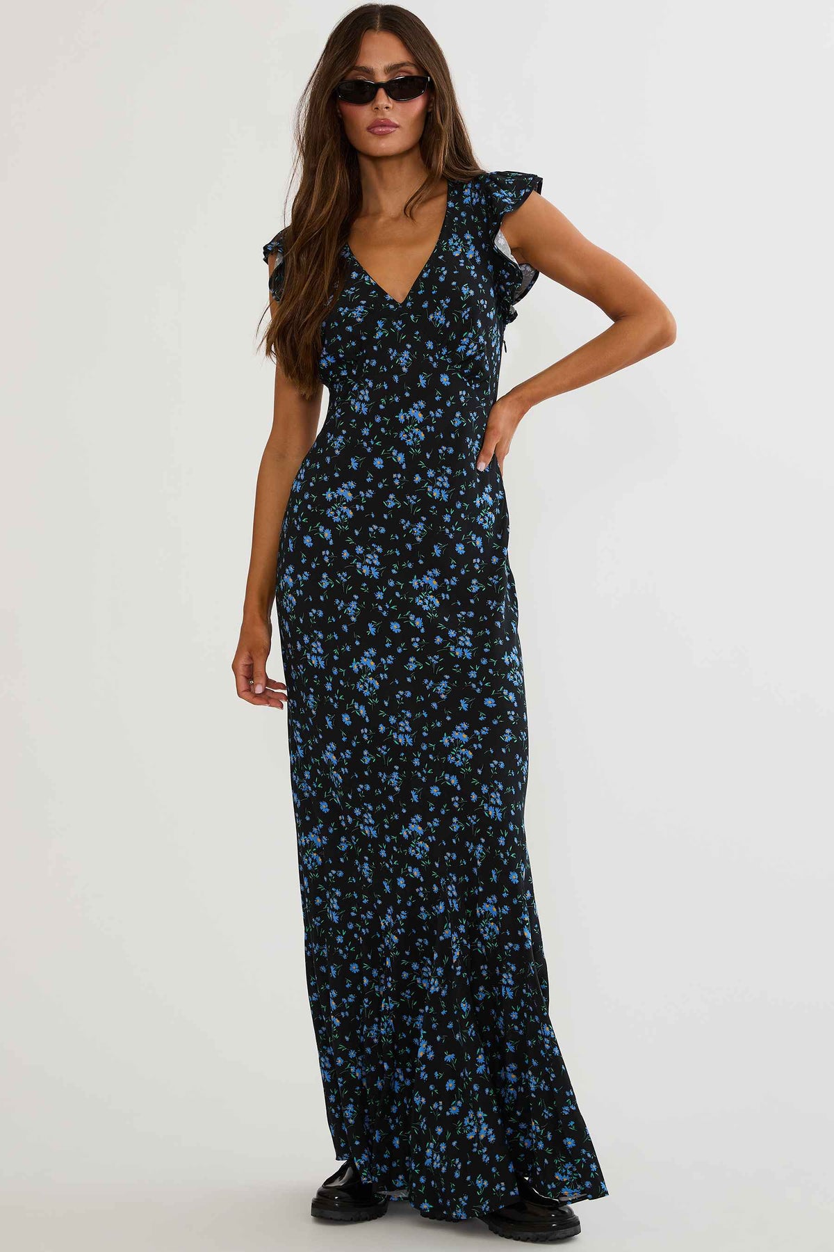 Woman wearing black maxi dress with blue florals on a white background. 