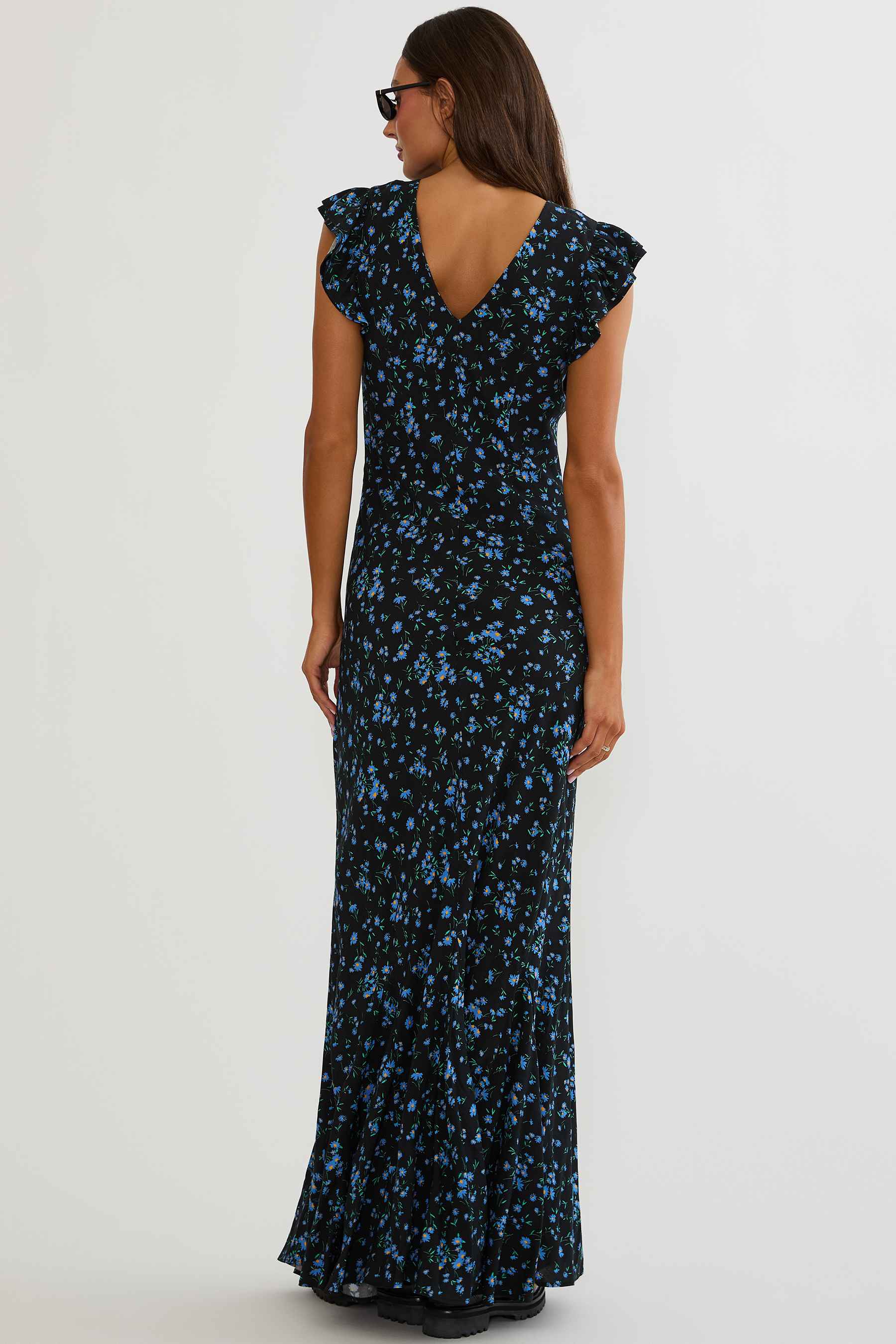 Woman wearing black maxi dress with blue florals on a white background. 