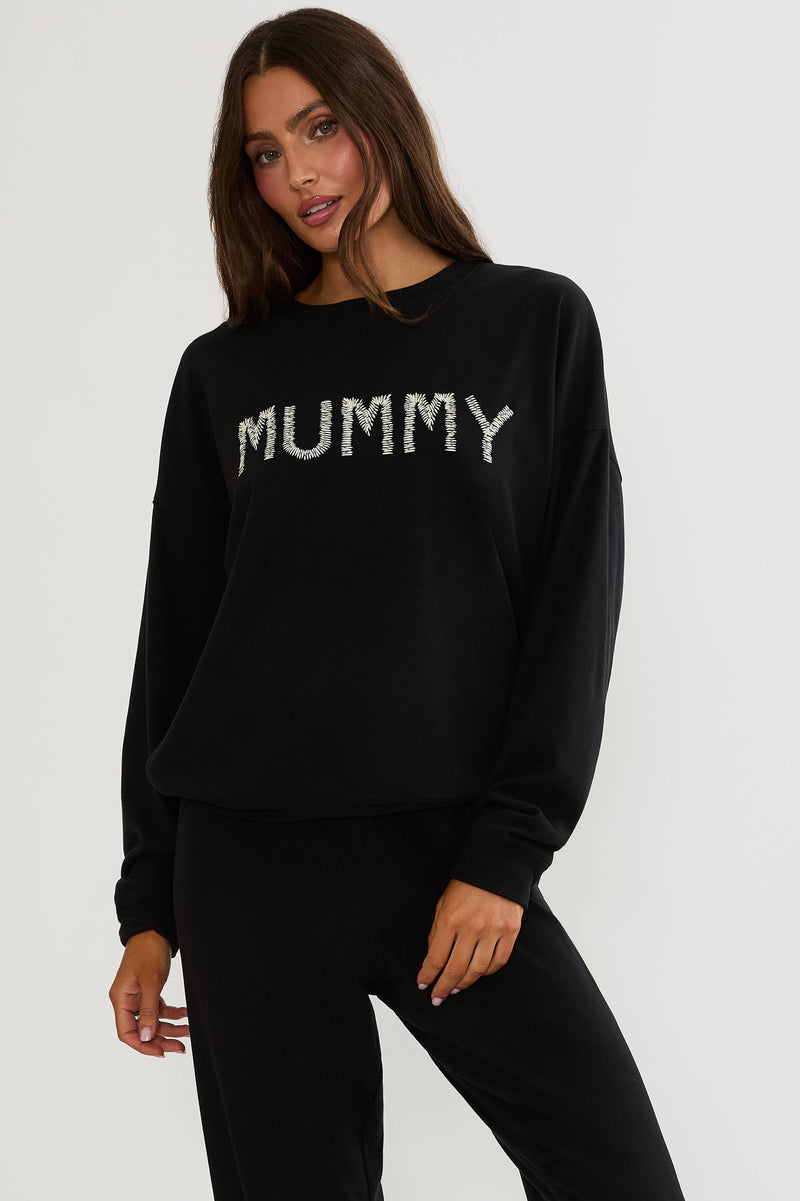Black oversized sweatshirt with Halloween text "mummy" worn by a woman on a plain white background. 