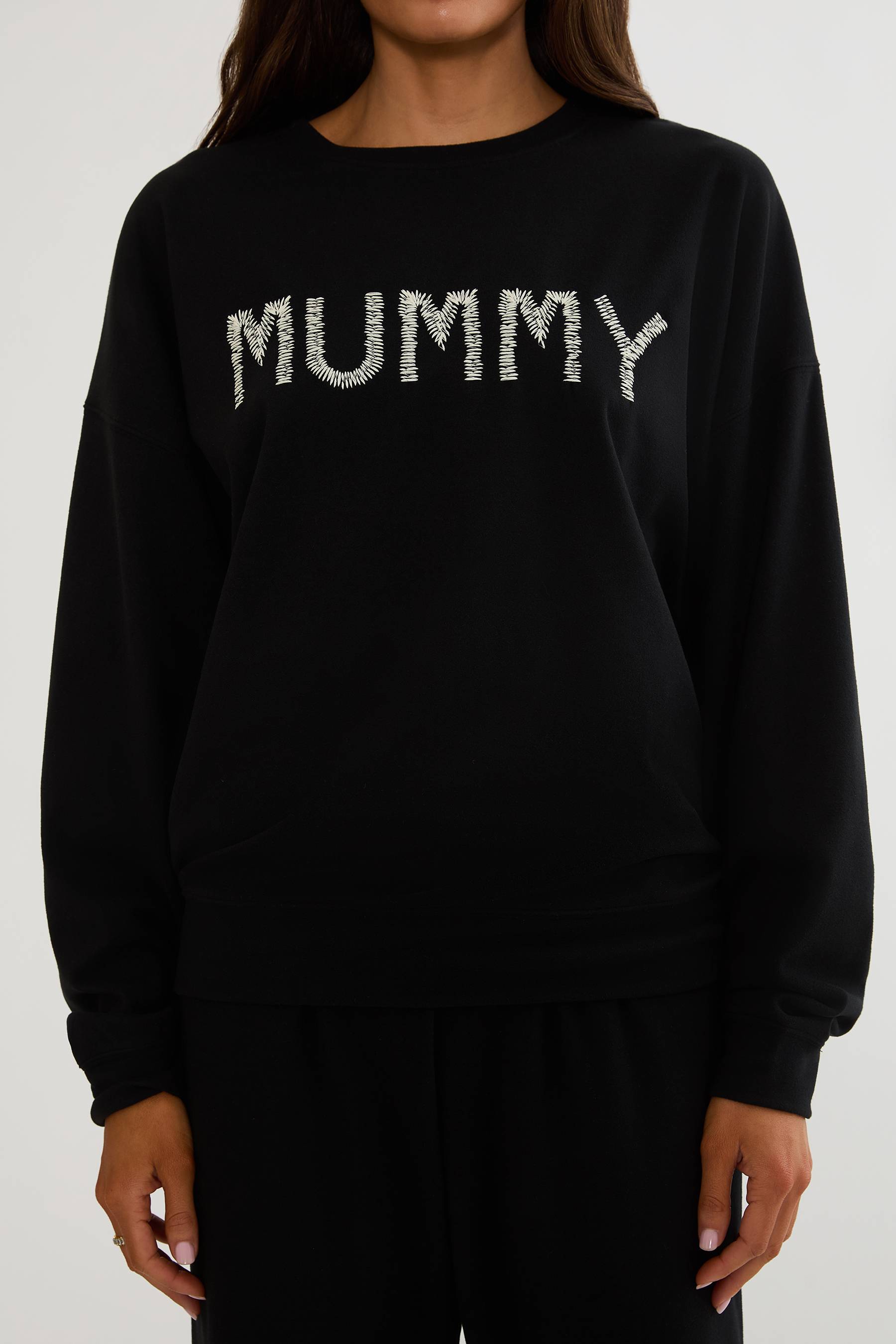Black oversized sweatshirt with Halloween text "mummy" worn by a woman on a plain white background. 