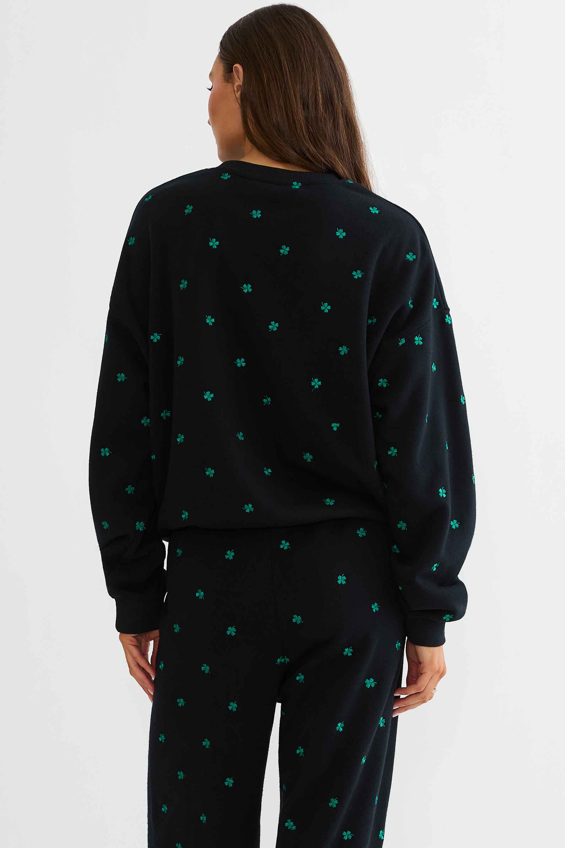 Person wearing a black sweater with green pattern on a white background