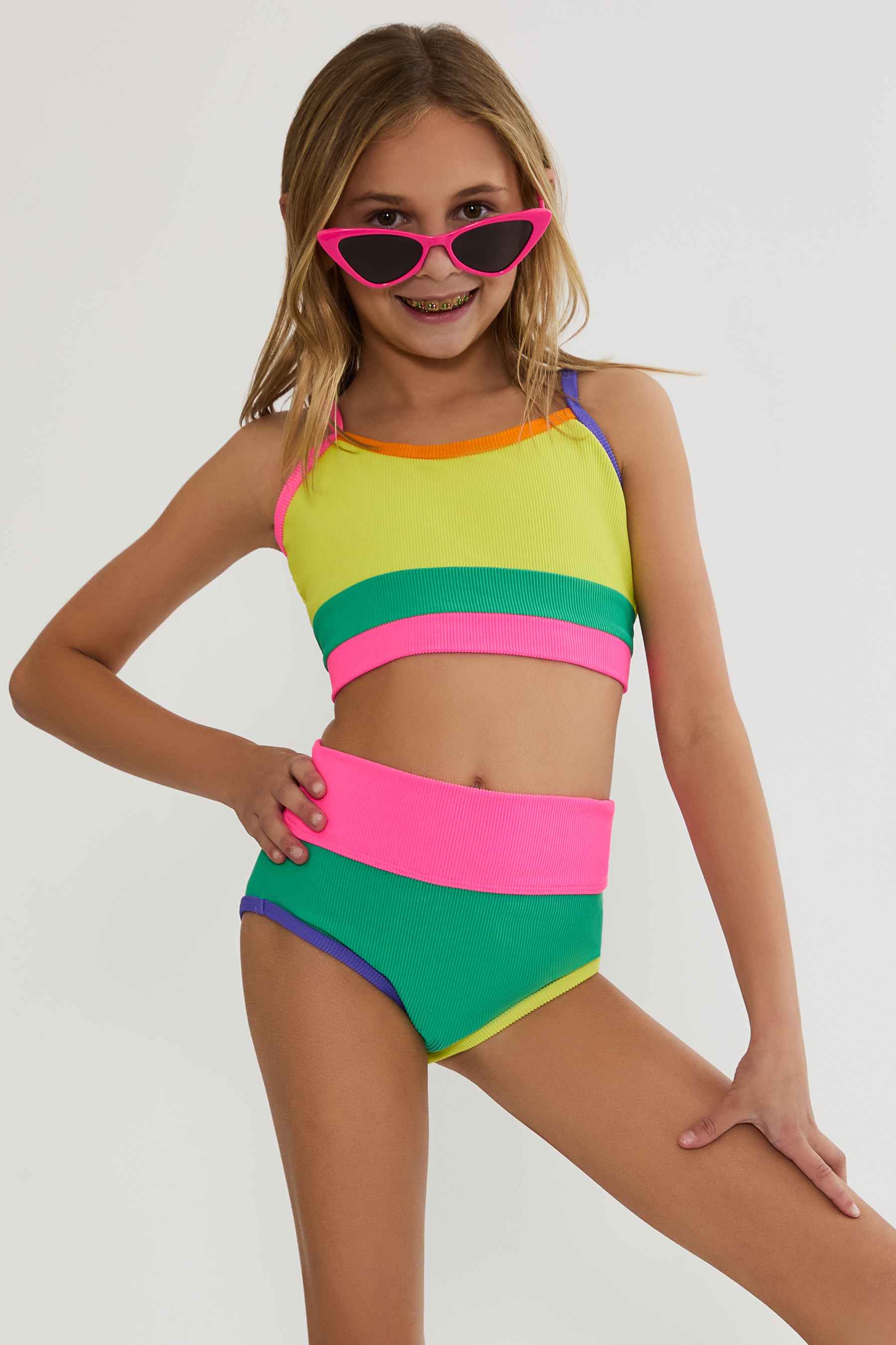 Young girl wearing a colorful two-piece swimsuit and pink sunglasses on a white background