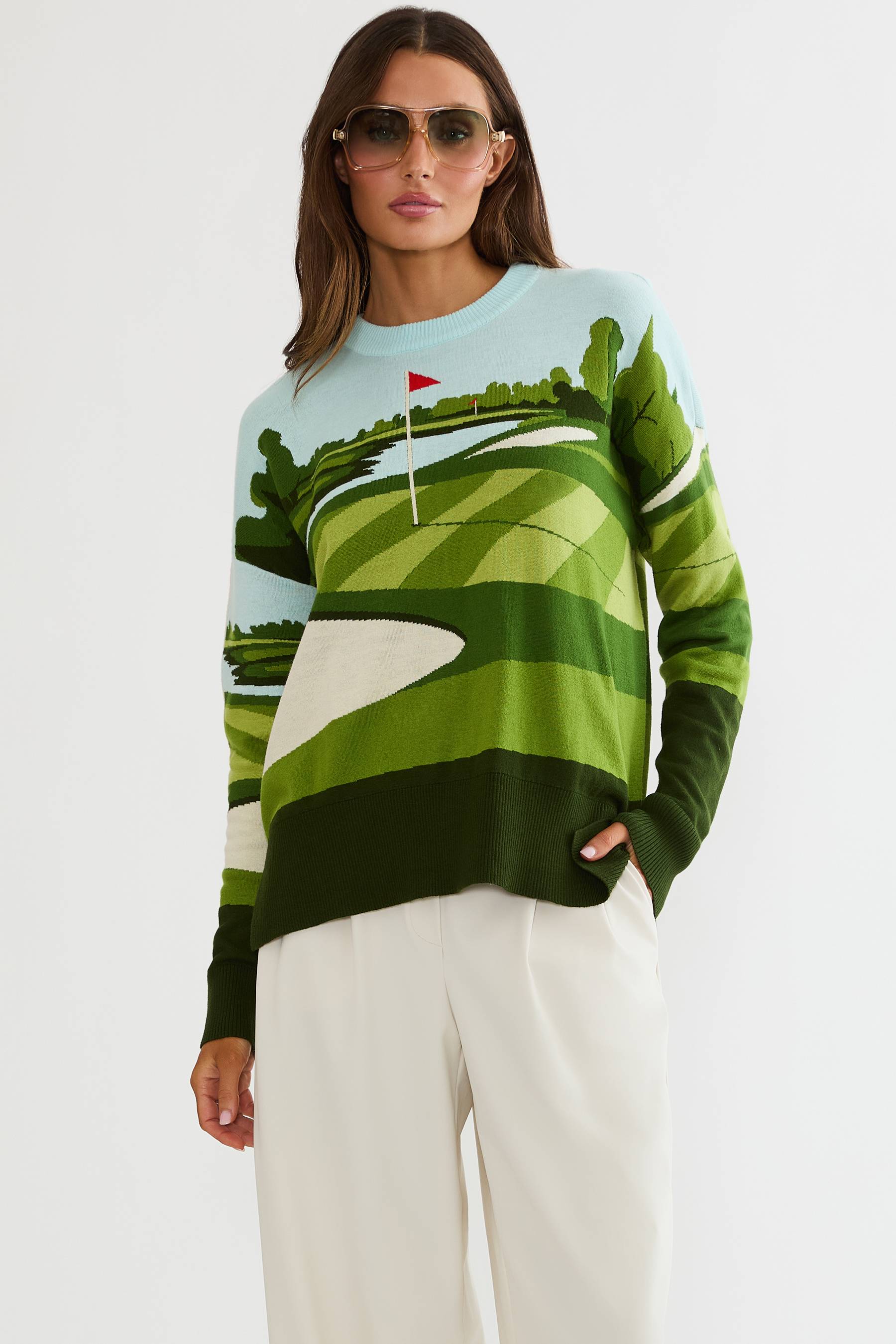 Woman wearing a green and white patterned sweater with a golf course design on a plain background