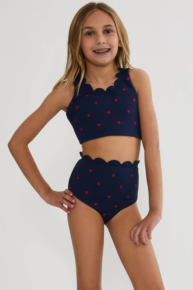 Young girl wearing a navy blue bikini with red star patterns on a white background
