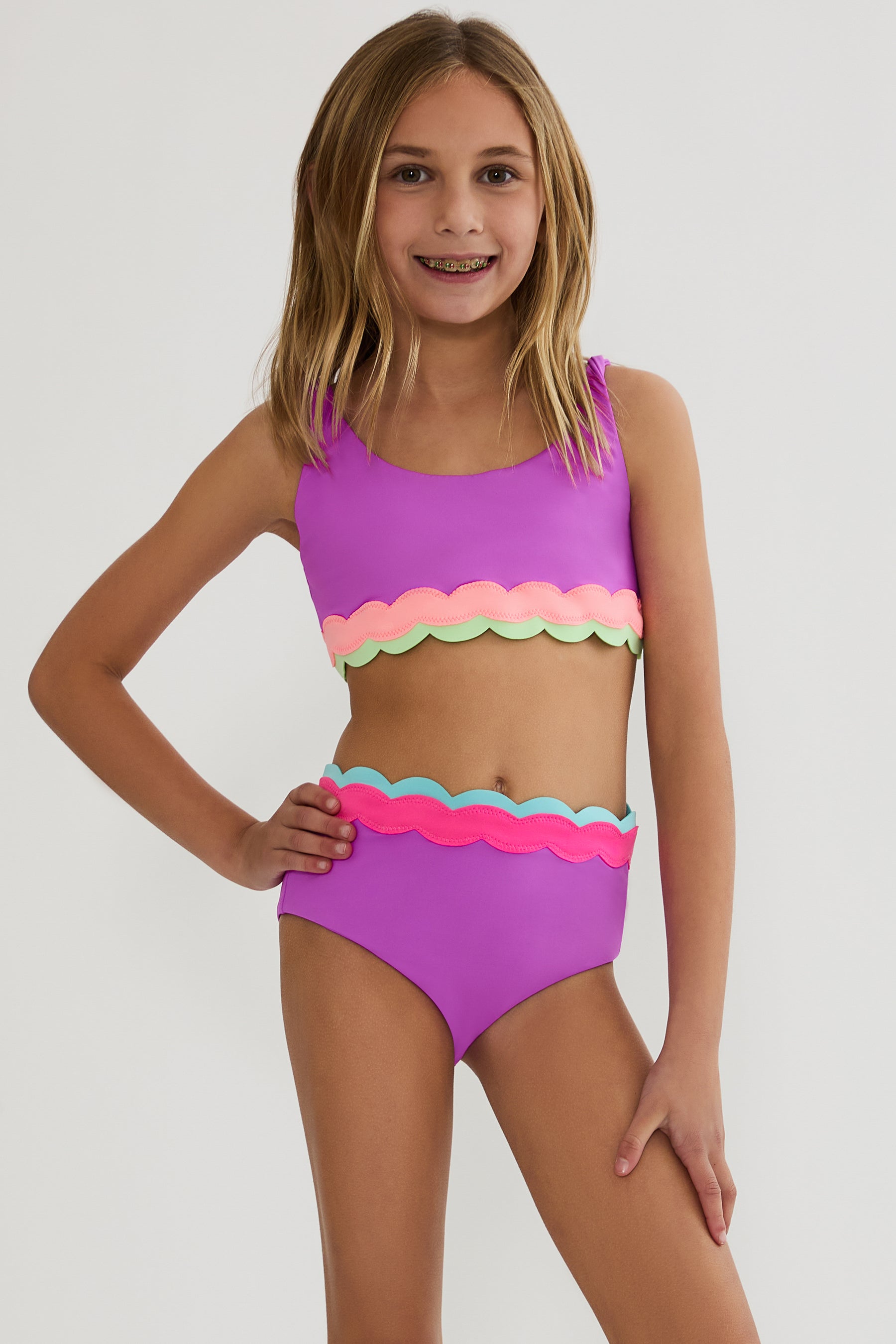 Young girl wearing a colorful two-piece swimsuit on a plain background